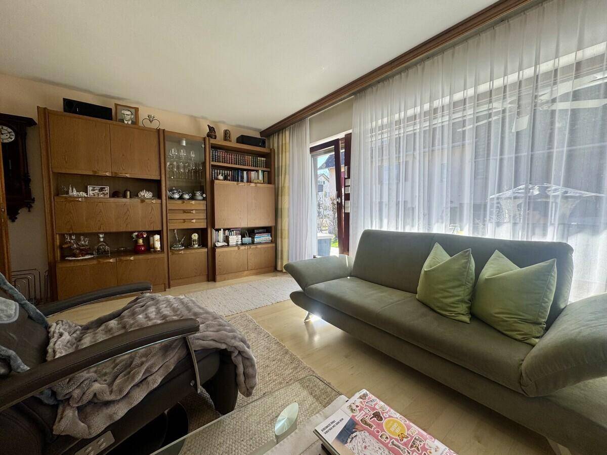 Wohnzimmer mit Sofa, Holzschränken und Zugang zu einem sonnigen Außenbereich.
