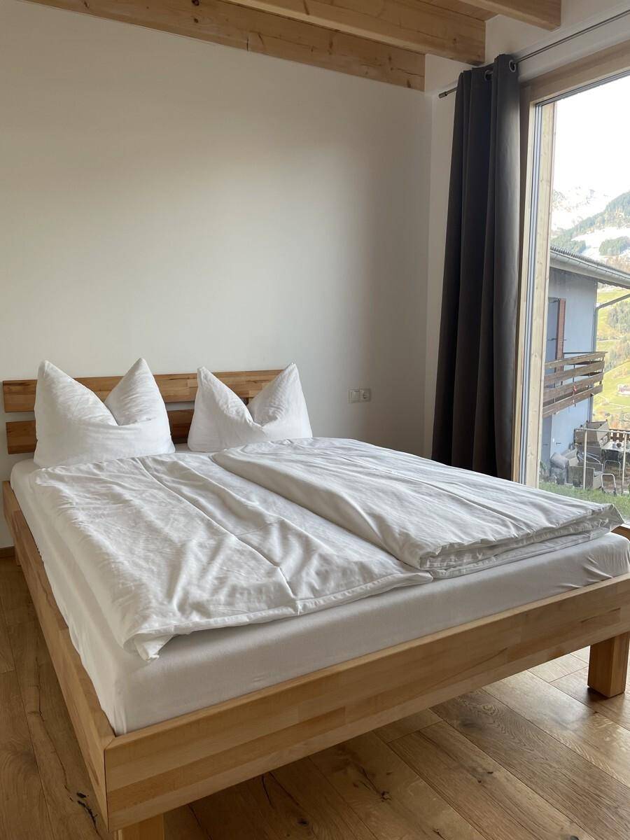 Gemütliches Schlafzimmer mit hellem Holzbett und weißer Bettwäsche, gut beleuchtet.