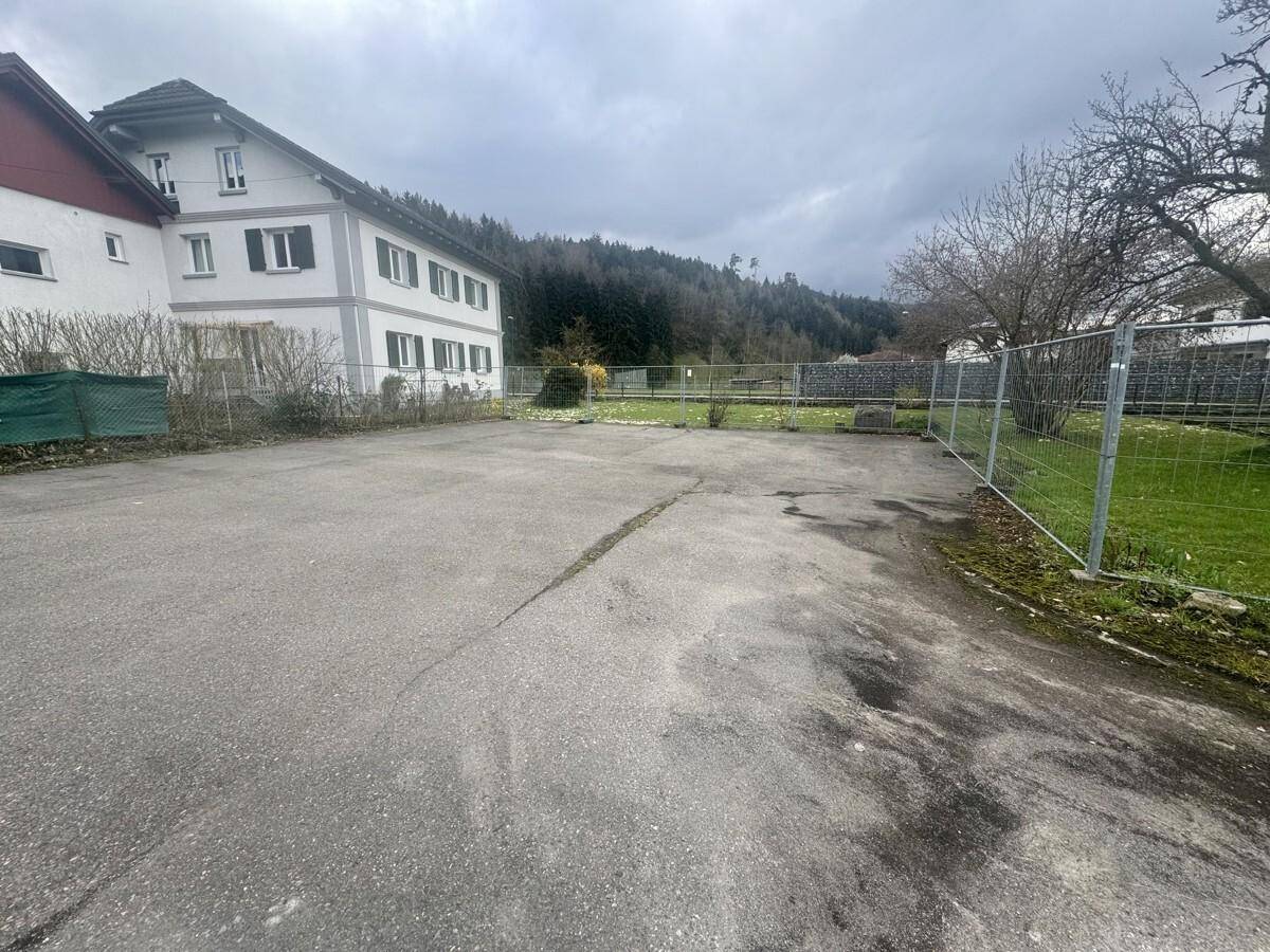 Weitläufiges Grundstück mit älterem Gebäude im Hintergrund und bewaldeter Hügellandschaft.