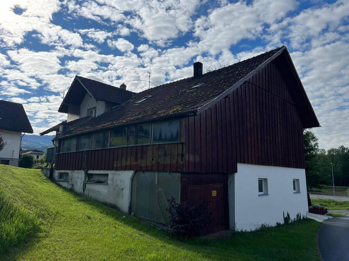 Seitenansicht des Hauses mit Holzfassade, Satteldach und Hanglage, umgeben von grüner Natur.