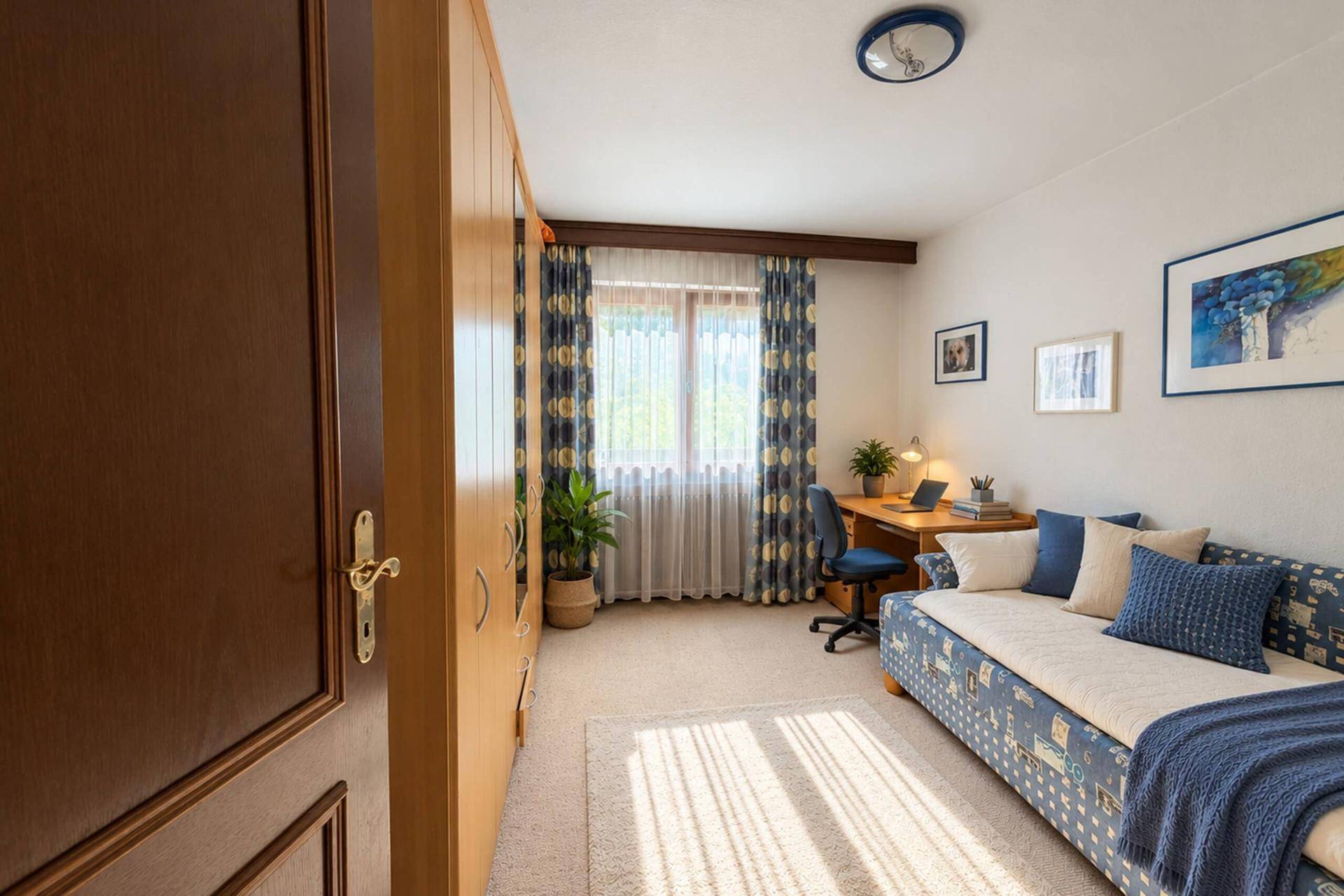 Gemütliches Schlafzimmer mit Teppichboden, Schrank und Fenster mit Blick ins Grüne.