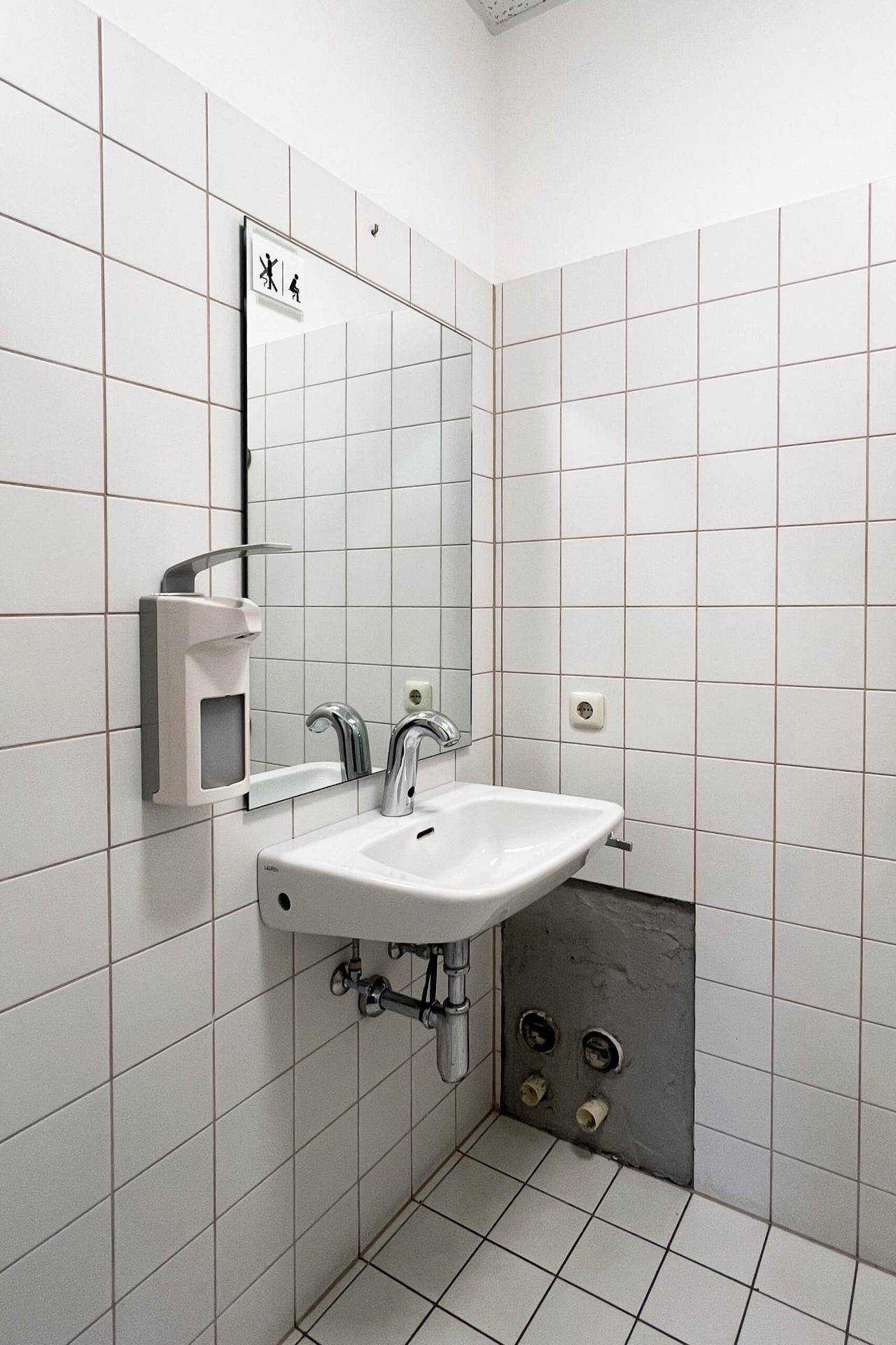 Helles Badezimmer mit Waschbecken, Spiegel und weißen Fliesen, funktional und sauber gestaltet.