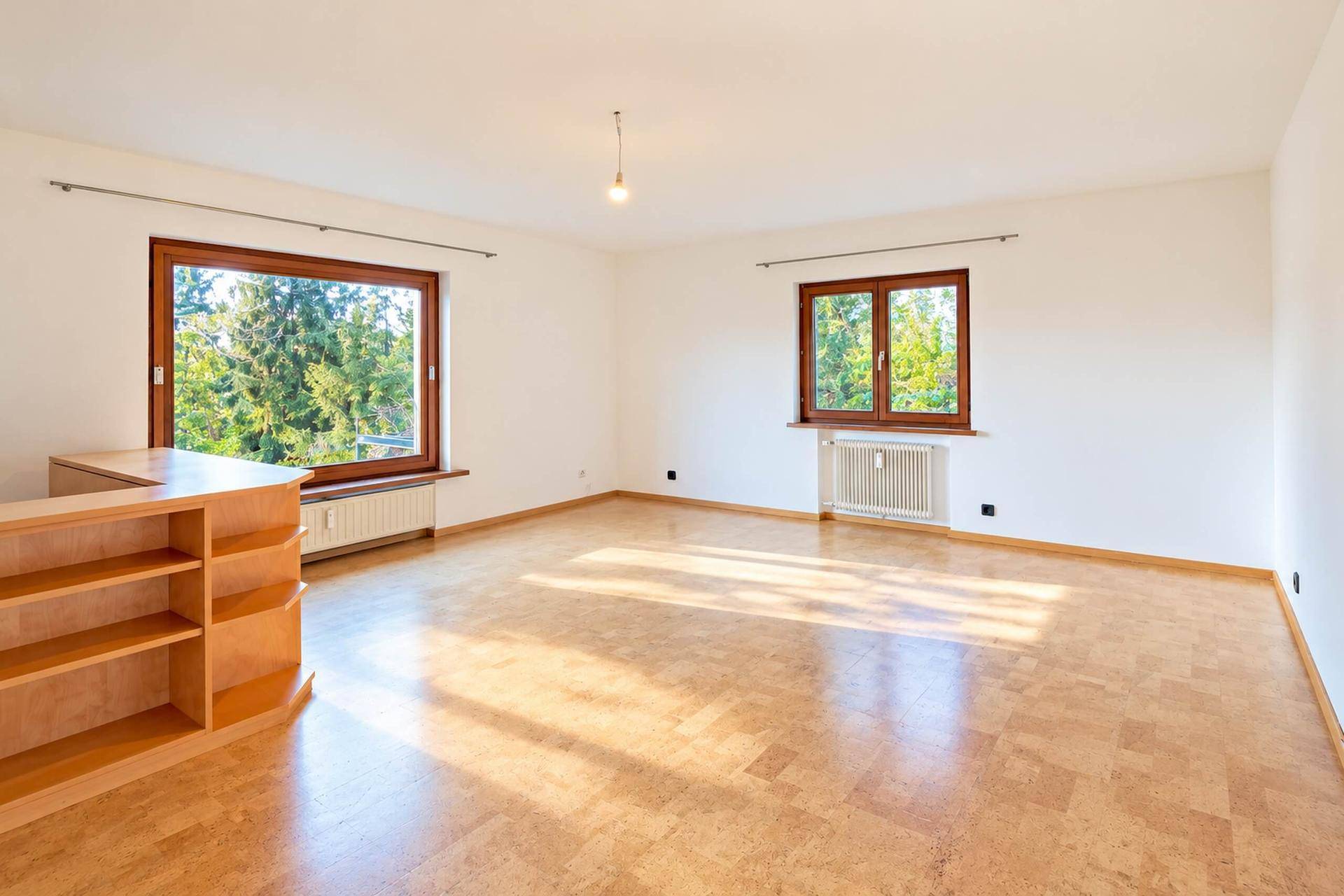 Helles Wohnzimmer mit Korkboden und großen Fenstern, die viel Tageslicht hereinlassen.
