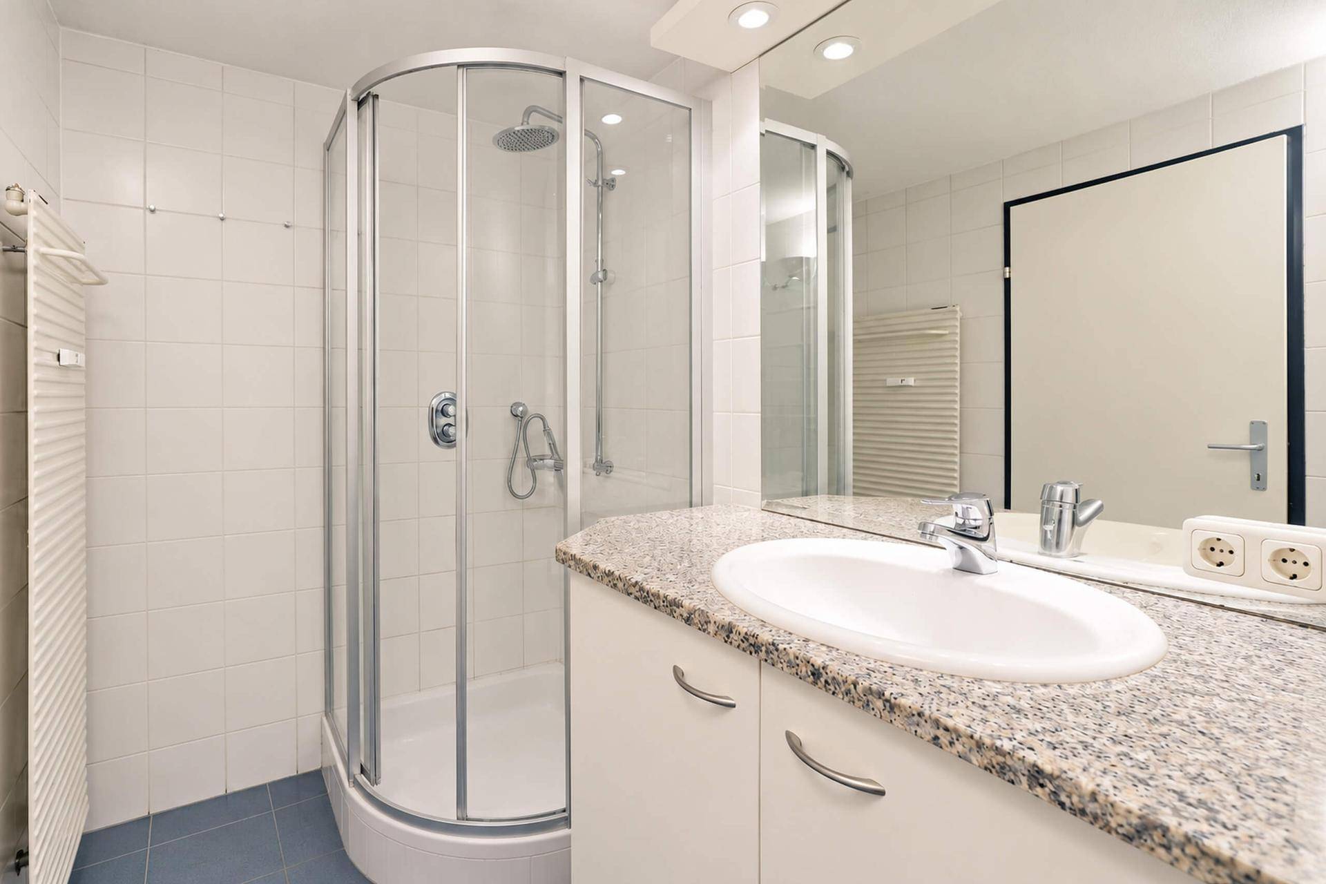 Modernes Badezimmer mit Duschkabine, Granitwaschtisch und weiß gefliesten Wänden.