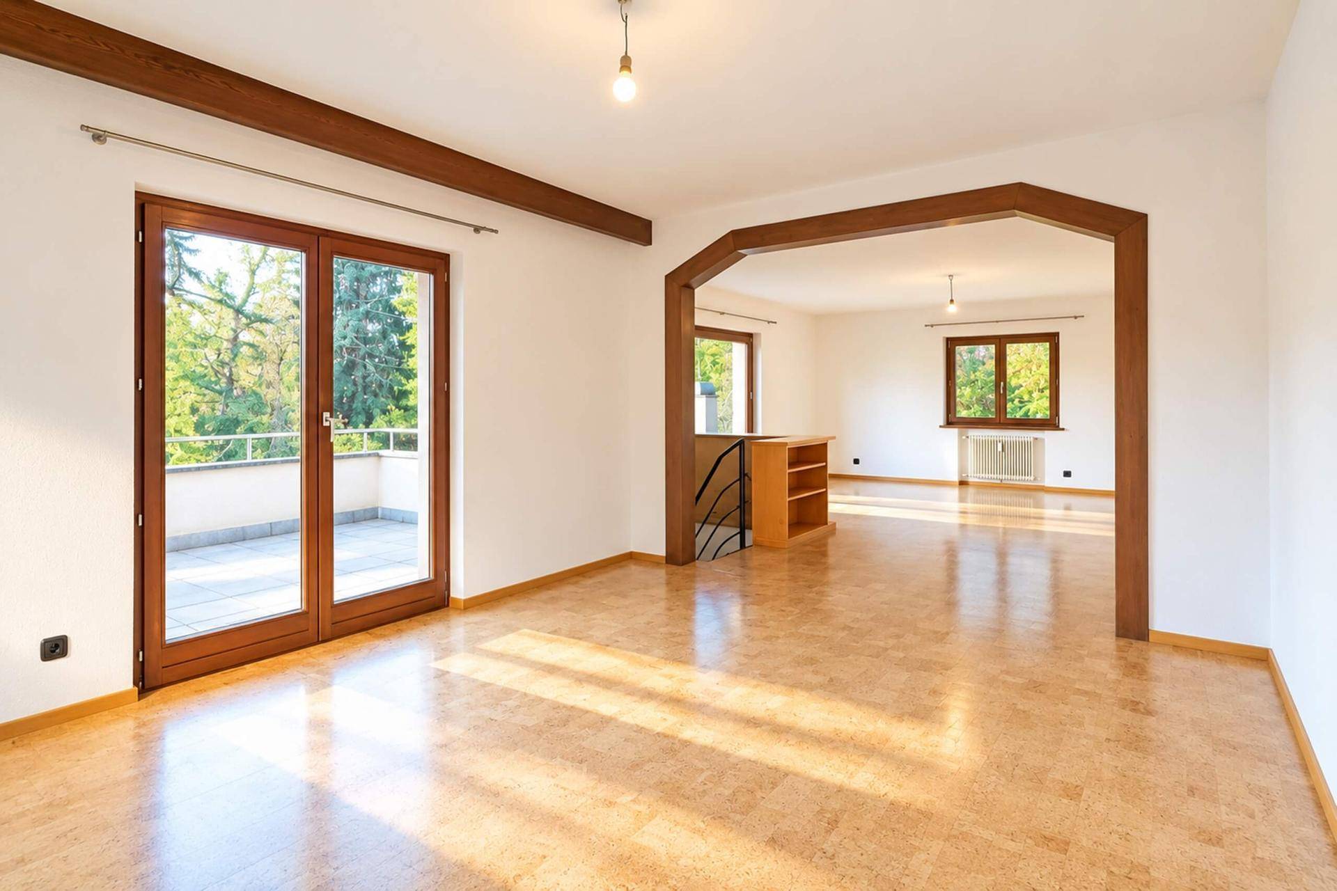 Geräumiges Wohnzimmer mit Korkboden, Holzbalken und Zugang zu einem sonnigen Balkon.