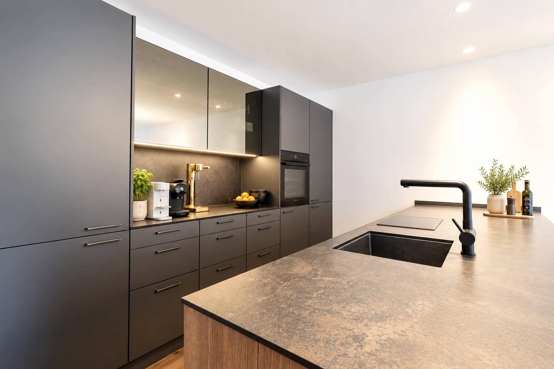 Moderne Küche mit dunklen, matten Fronten, integrierten Geräten und einer Arbeitsplatte in Steinoptik.