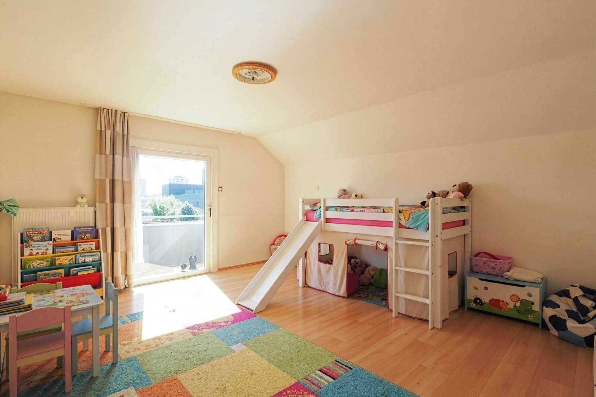 Kinderzimmer mit Hochbett, bunter Teppich und Zugang zum Balkon, spielerisch gestaltet.