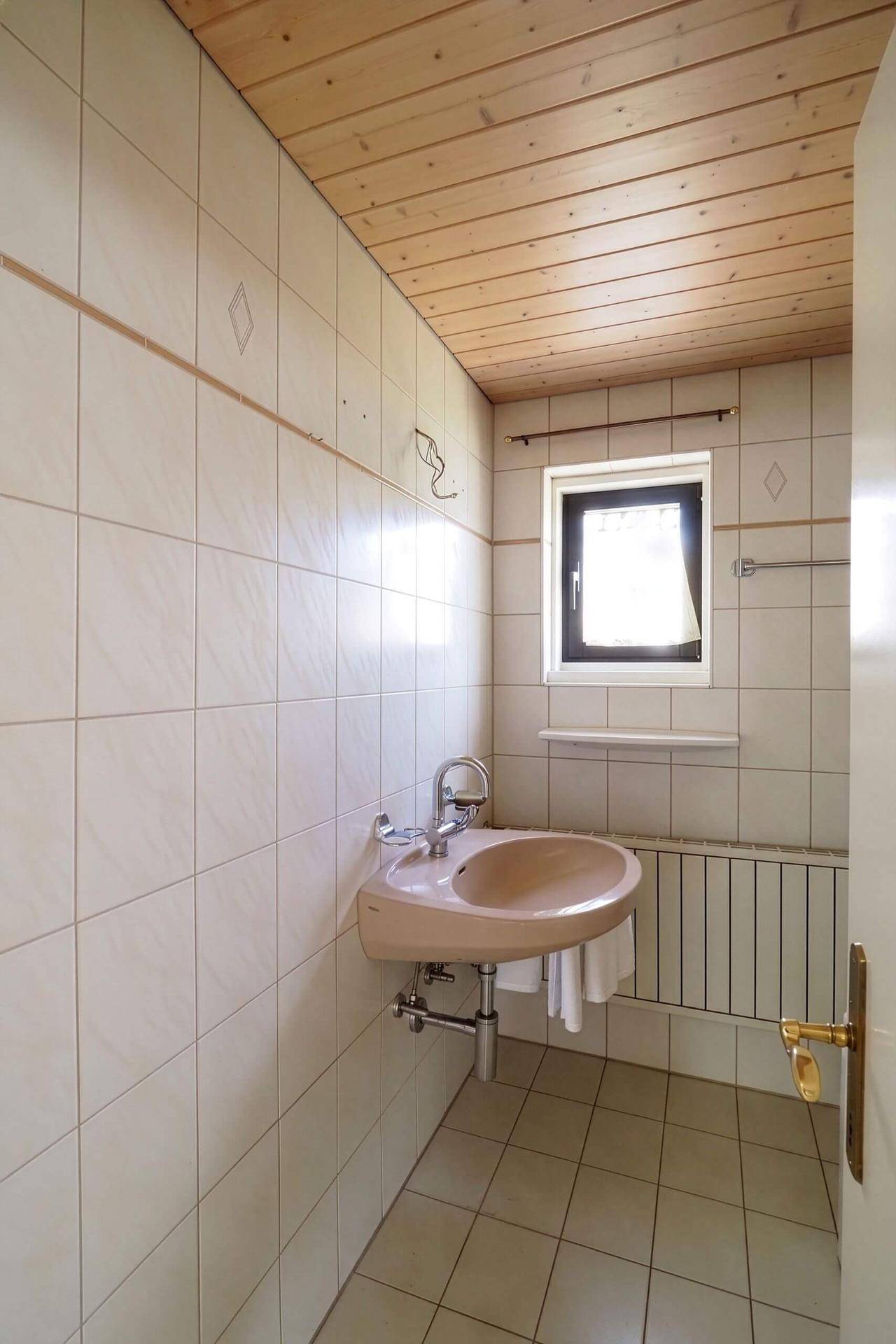 Badezimmer im 80er-Jahre-Stil mit beigem Waschbecken, Fliesen und Holzdecke, funktional.