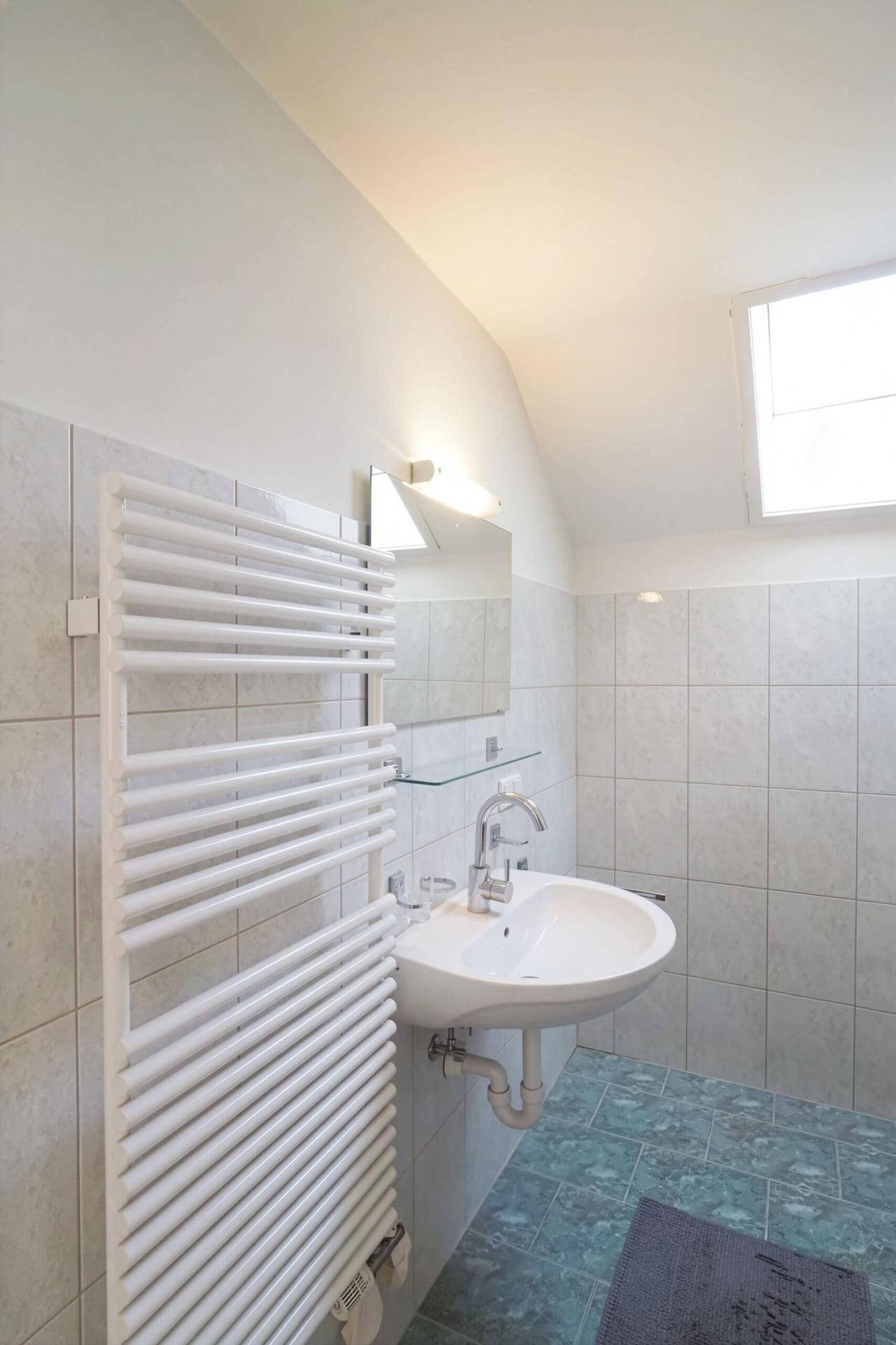 Modernisiertes Badezimmer mit Waschbecken, Handtuchheizkörper und Dachfenster, hell und funktional.