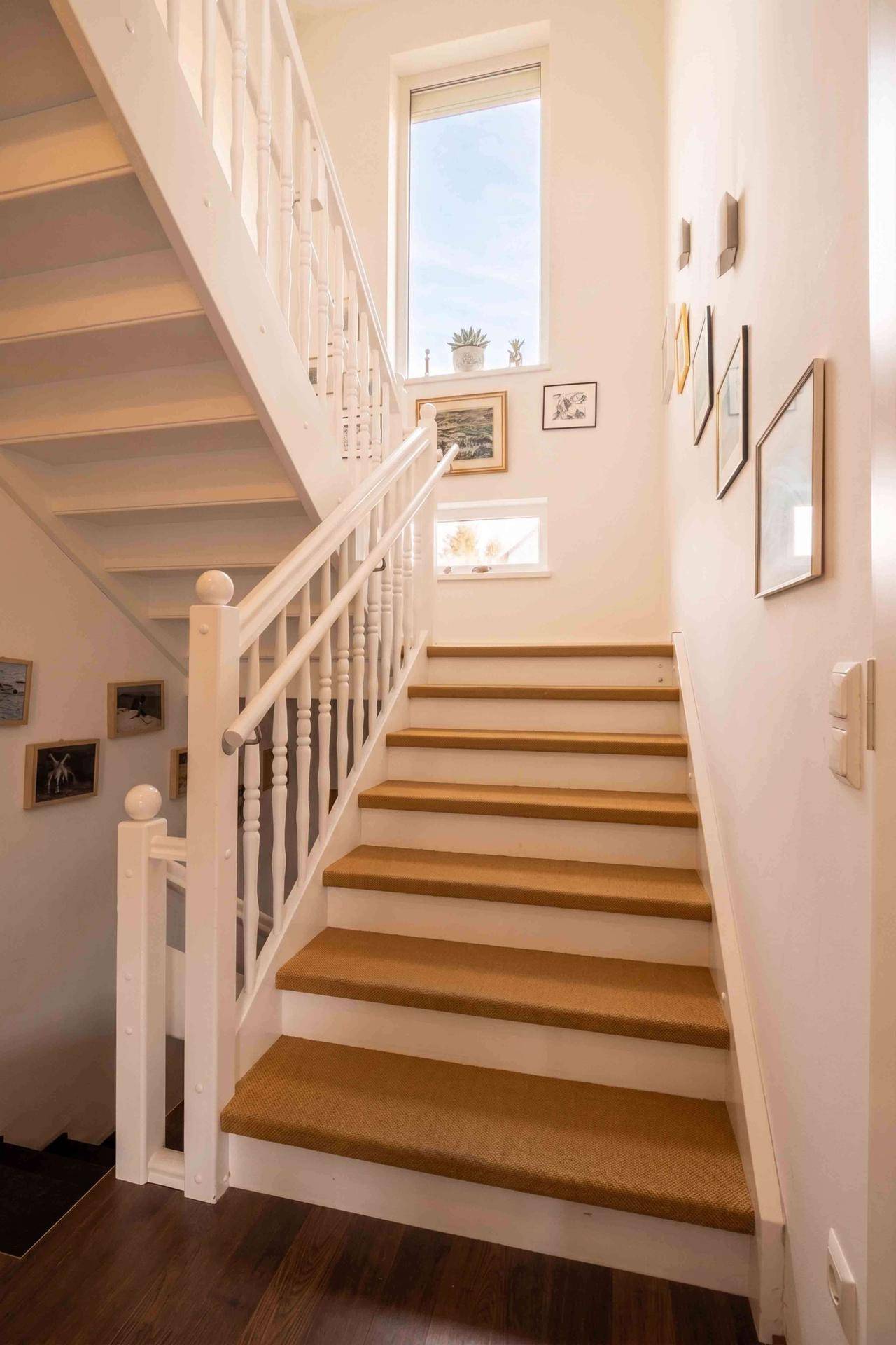 Helle Holztreppe mit weißem Geländer und Fenstern für natürliches Licht.