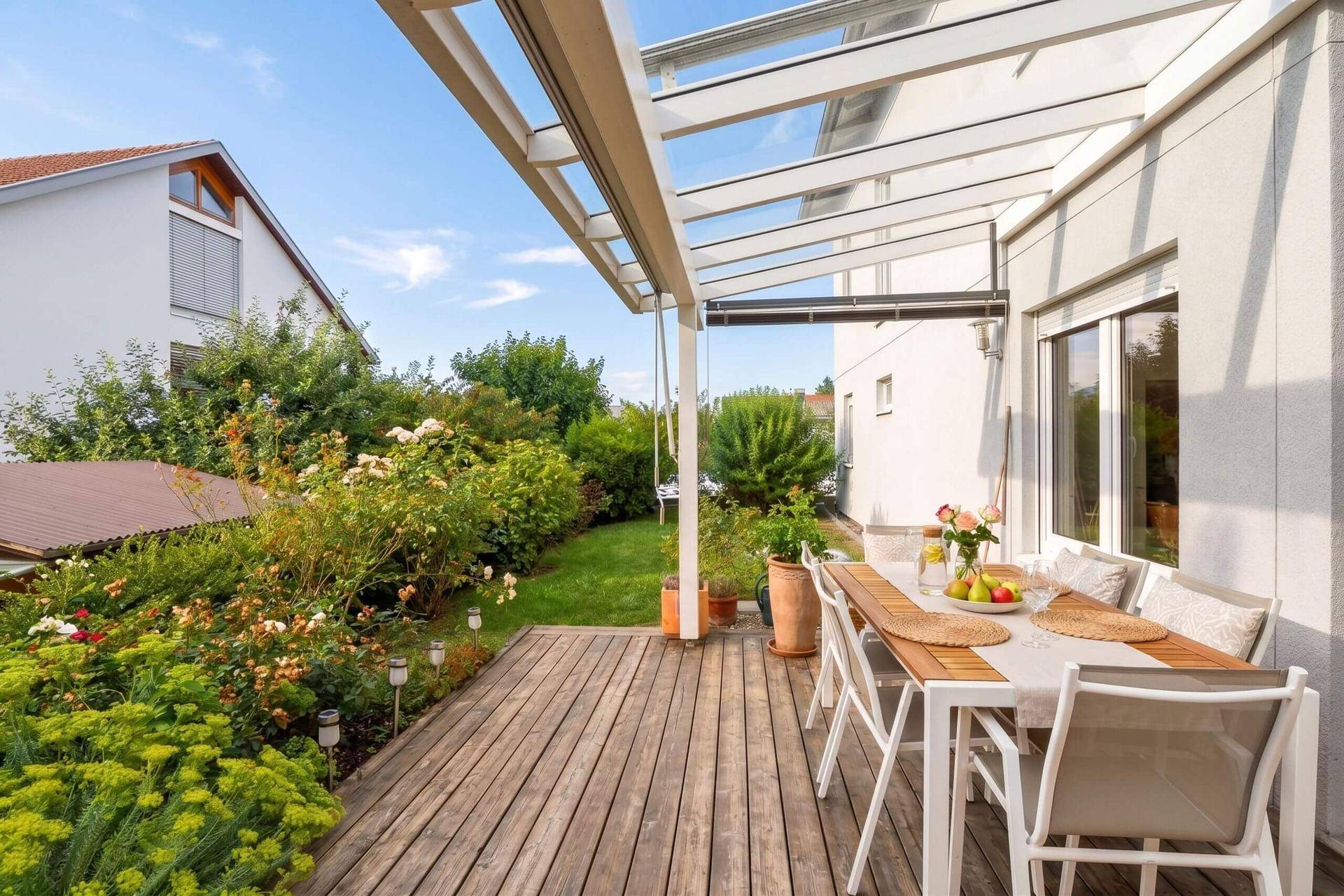 Große Holzterrasse mit Esstisch, Gartenmöbeln und Blick ins Grüne.