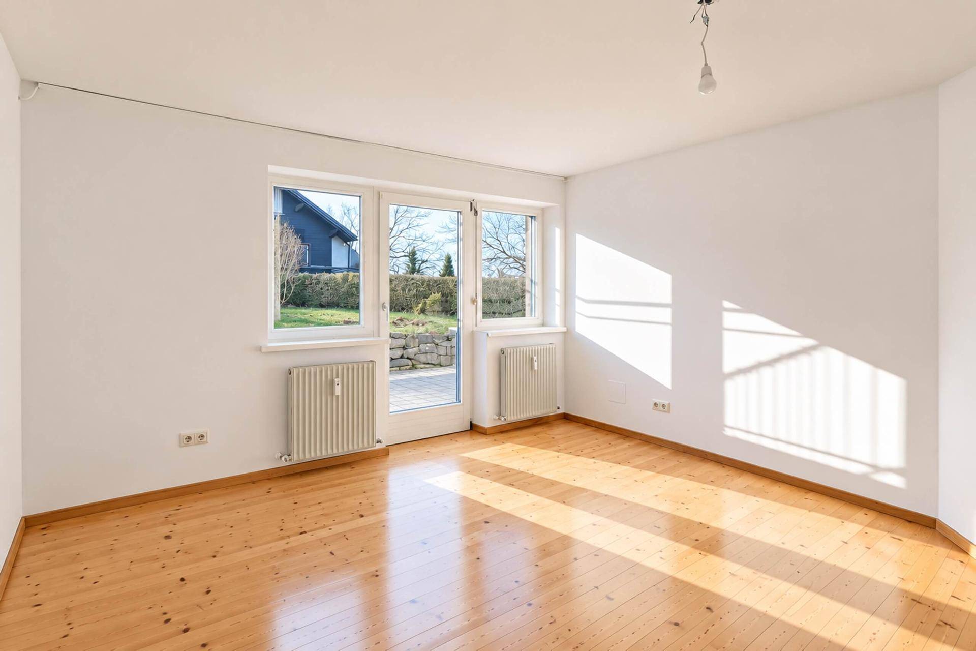 Lichtdurchflutetes Zimmer mit Holzparkettboden und Ausgang zu einer kleinen Terrasse im Garten.