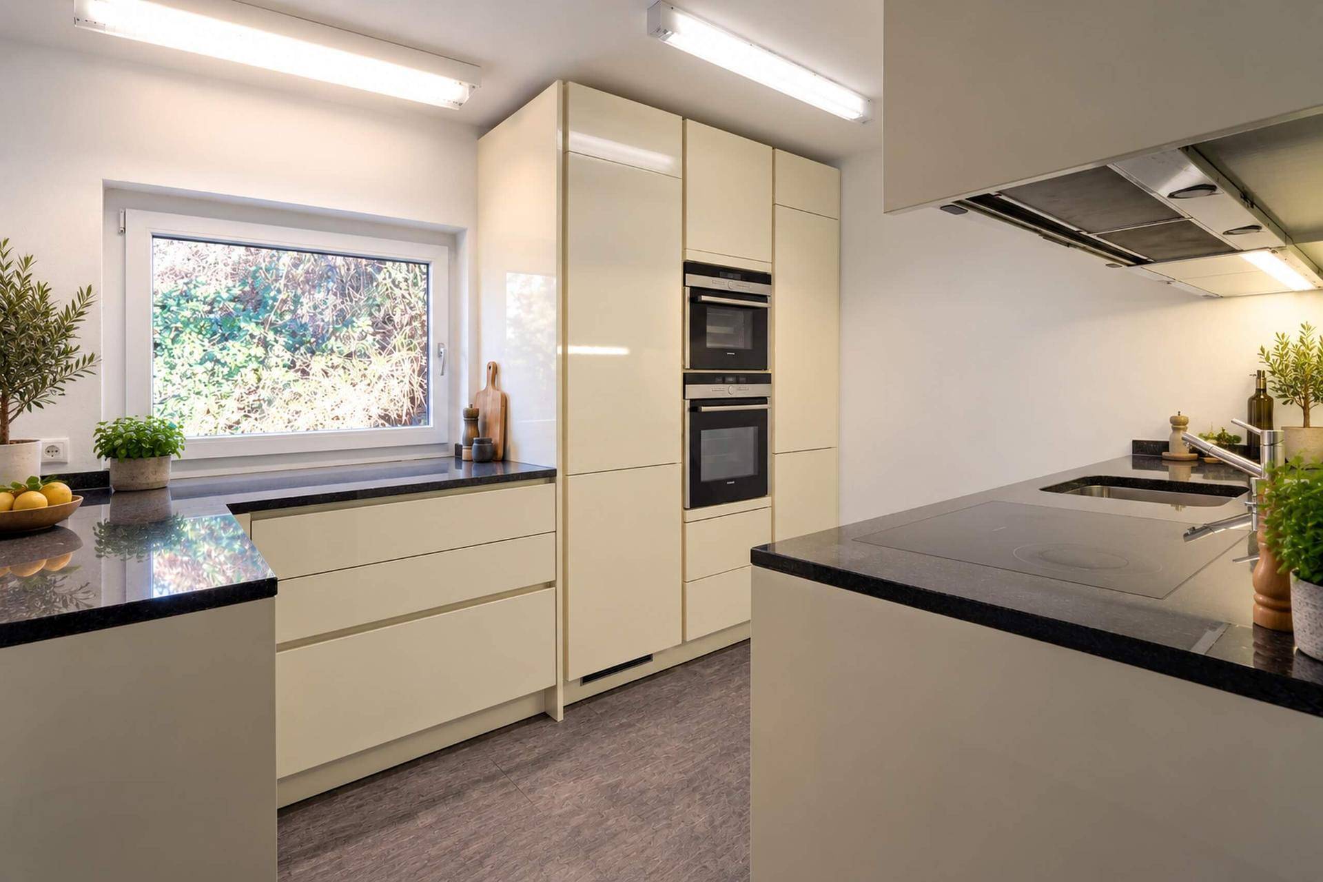 Moderne Küche mit cremefarbenen Hochglanzfronten, dunklen Arbeitsplatten und integrierten Geräten.