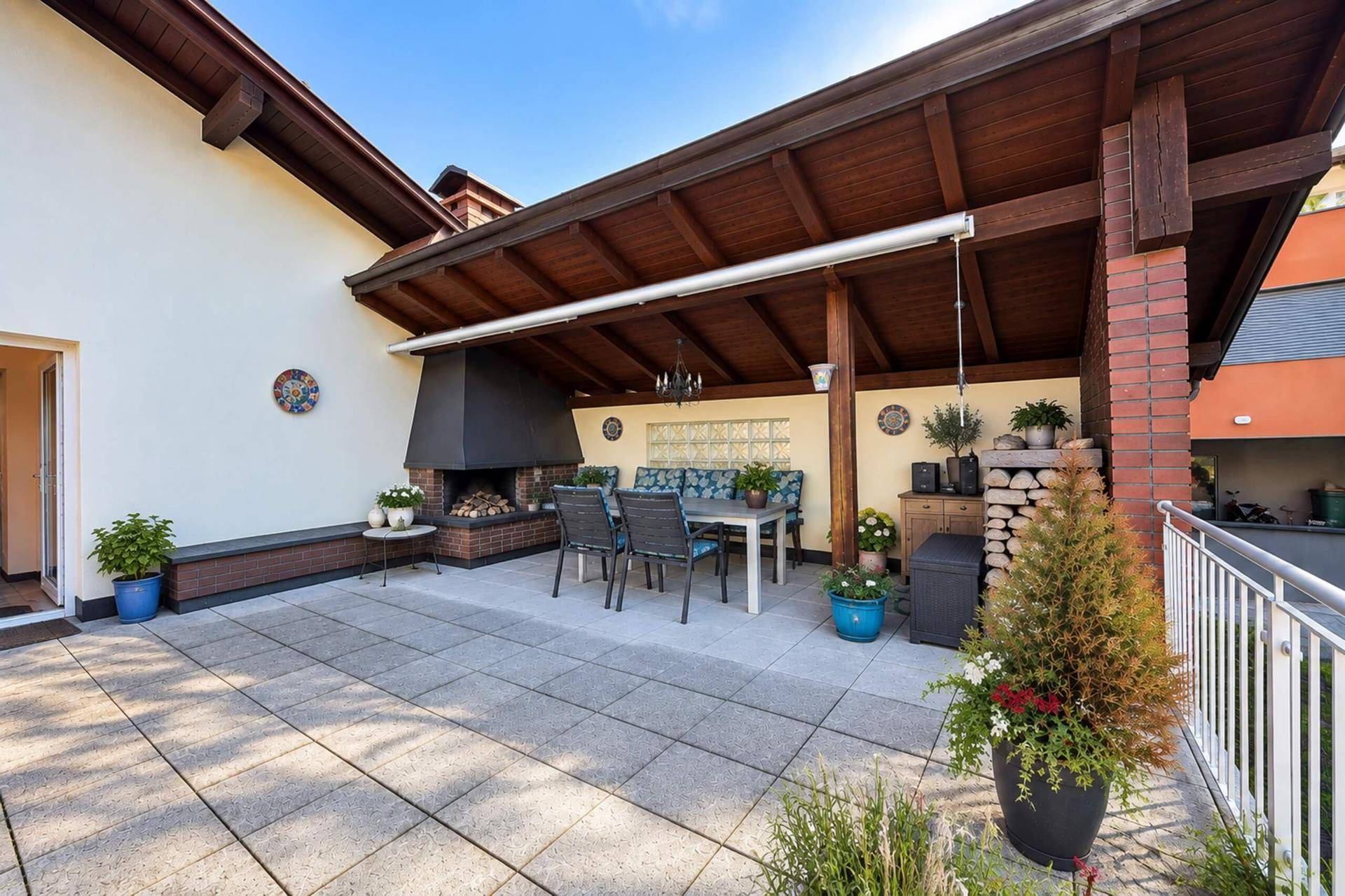Große überdachte Terrasse mit Außenkamin, Essbereich und Blick auf die Umgebung.