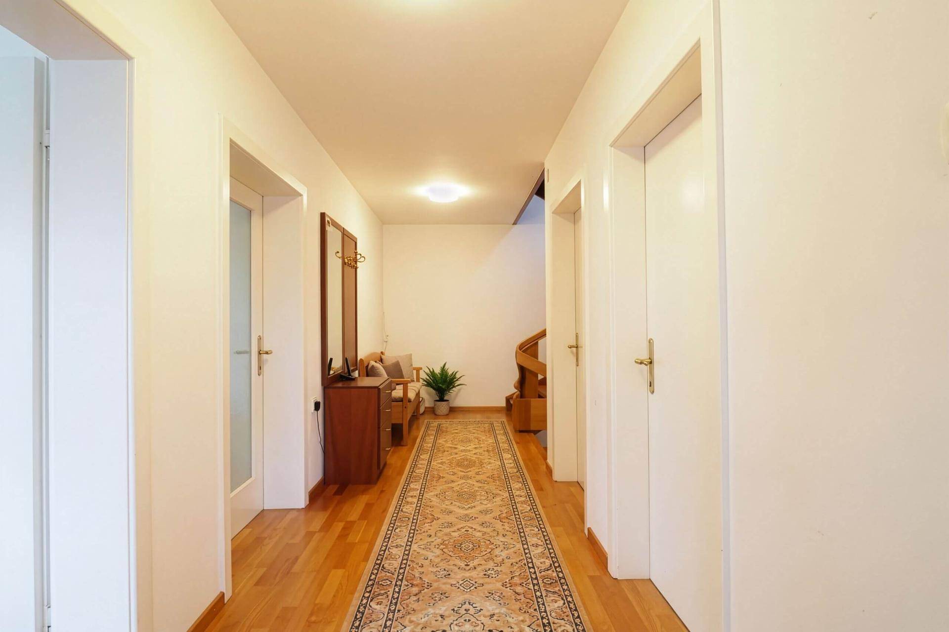Langer Flur mit Holzparkett, Teppichläufer und Garderobe, einladender Eingangsbereich.