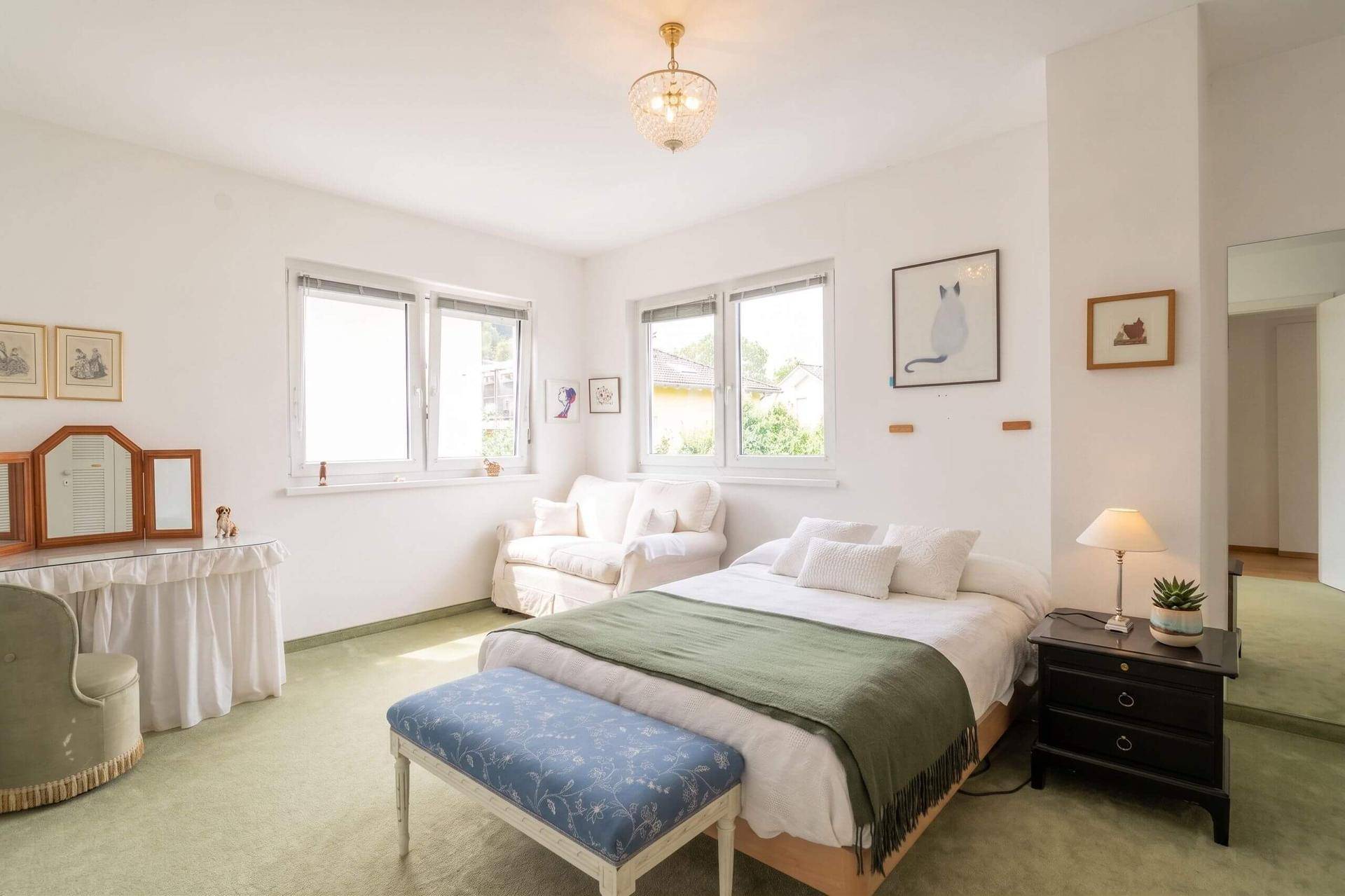 Helles Schlafzimmer mit grünem Teppichboden, Doppelbett und Fensterblick.