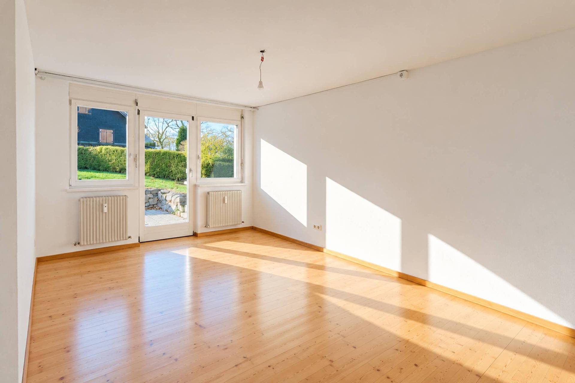 Helles Wohnzimmer mit Holzparkettboden und direktem Zugang zum Gartenbereich.