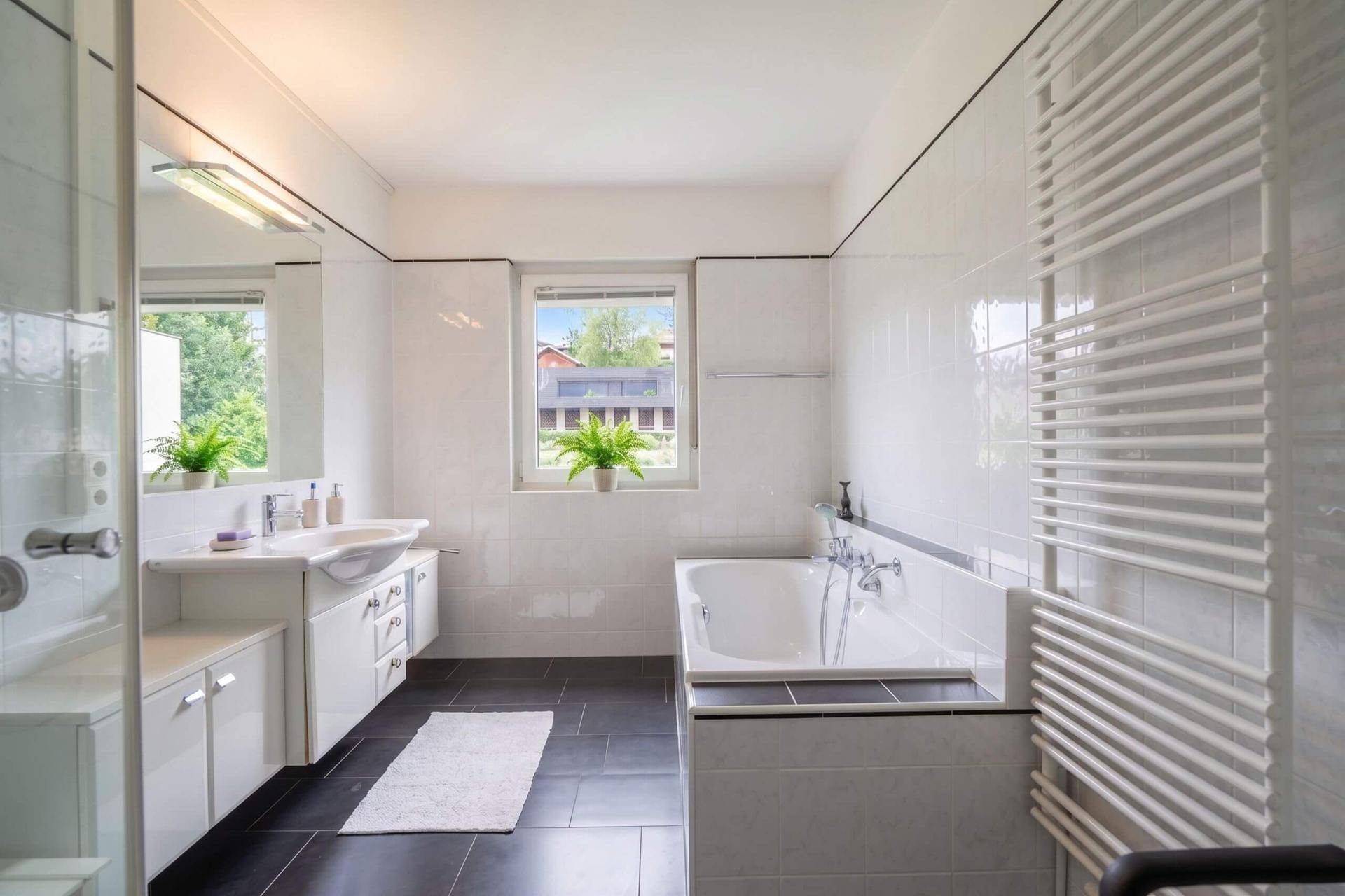 Modernes Badezimmer mit Badewanne, Dusche, dunklen Fliesen und Fenster.