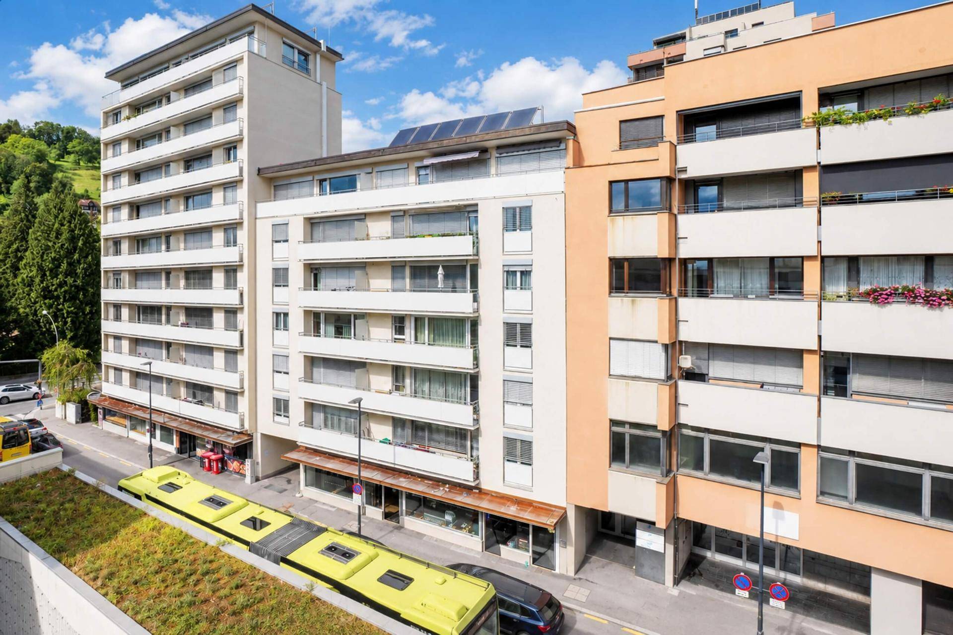 Mehrstöckiges Wohngebäude mit Balkonen und Geschäften im Erdgeschoss an einer Straße.