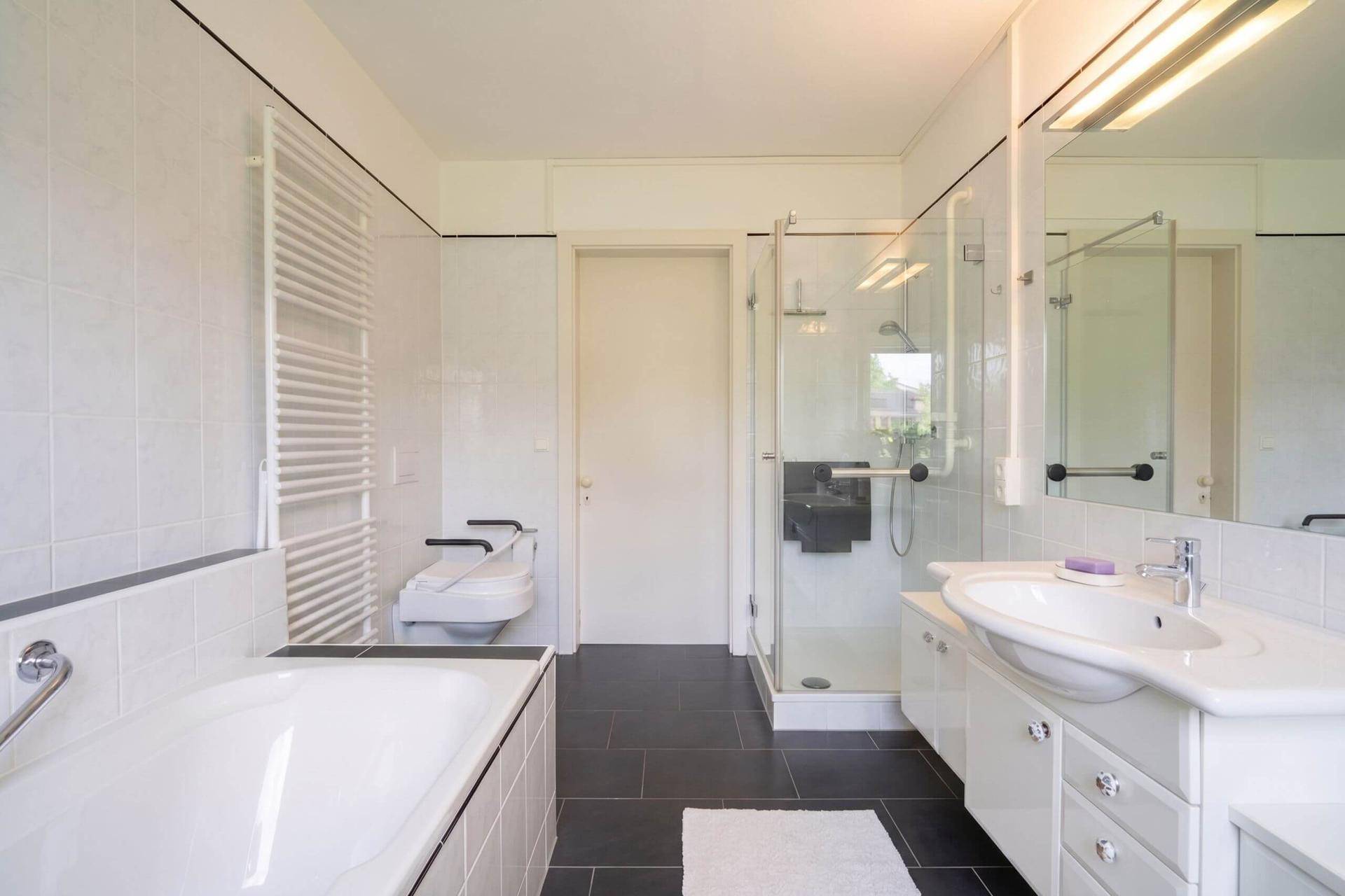 Barrierefreies Badezimmer mit Badewanne, ebenerdiger Dusche und Haltegriffen.