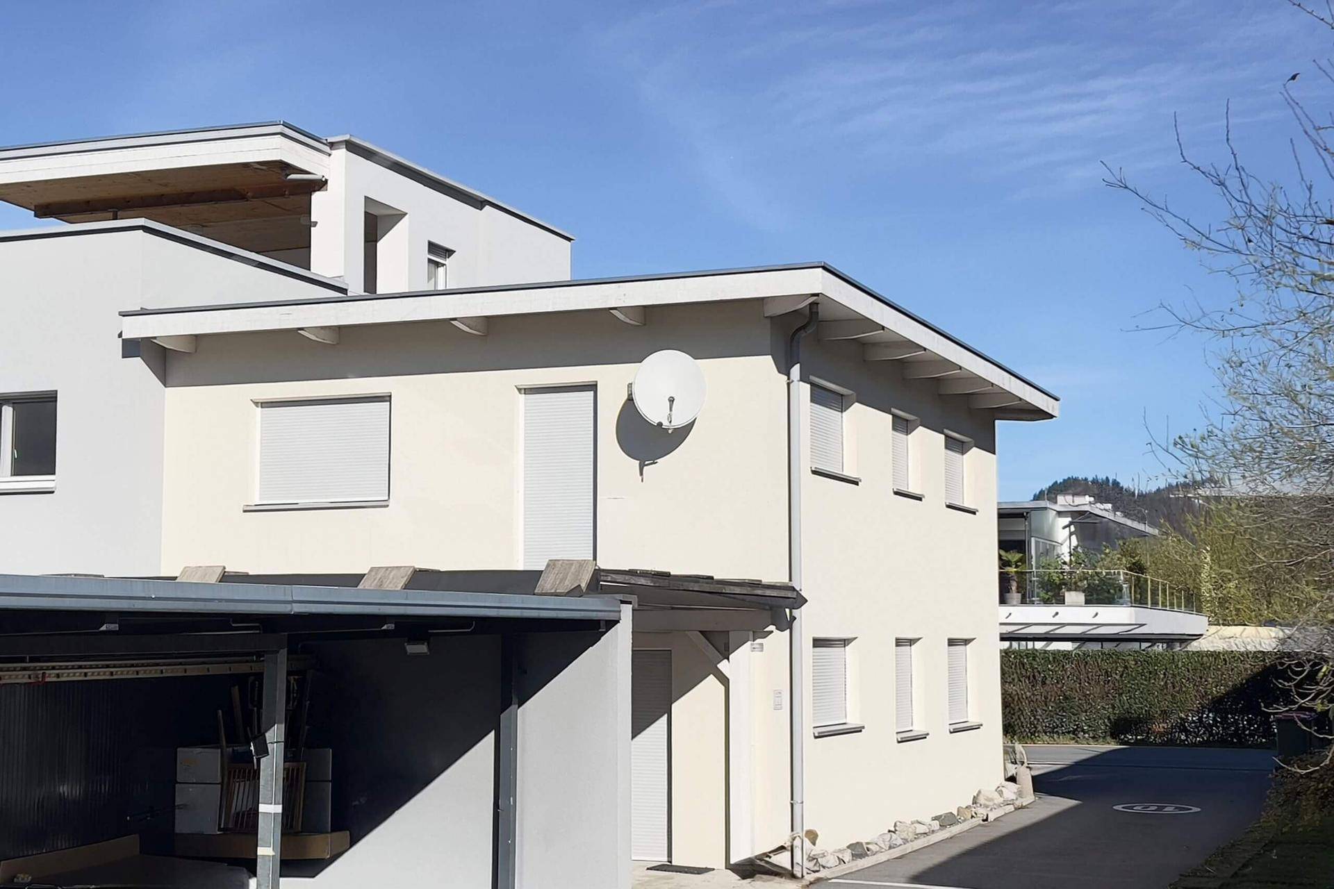Moderne Architektur mit heller Fassade, Flachdach und Rollläden an den Fenstern.