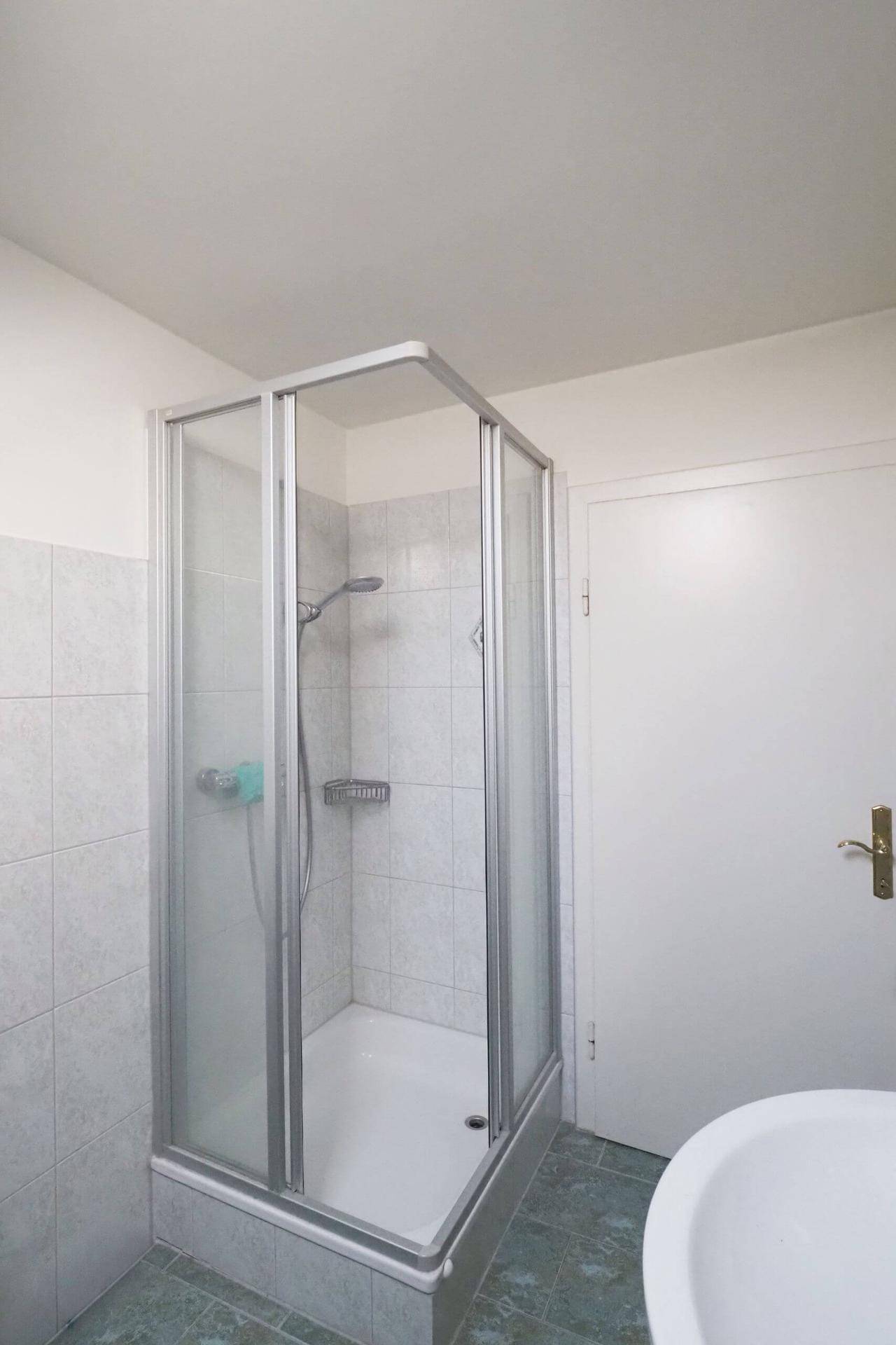 Badezimmer mit Duschkabine, Waschbecken und Fliesenboden, sauber und praktisch.