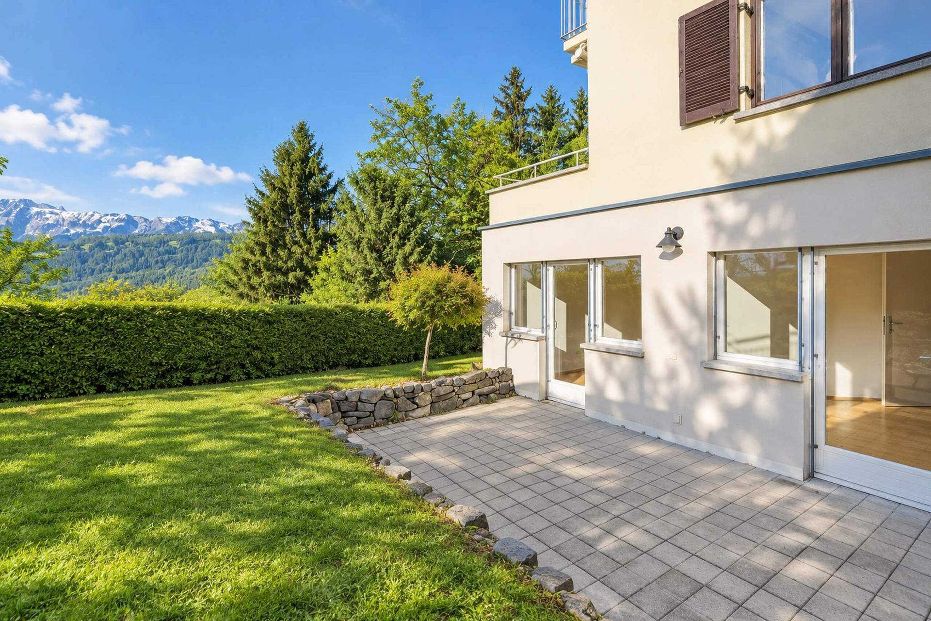 Gepflegter Gartenbereich mit Rasenfläche, Steinterrasse und Blick auf die umliegende Natur.