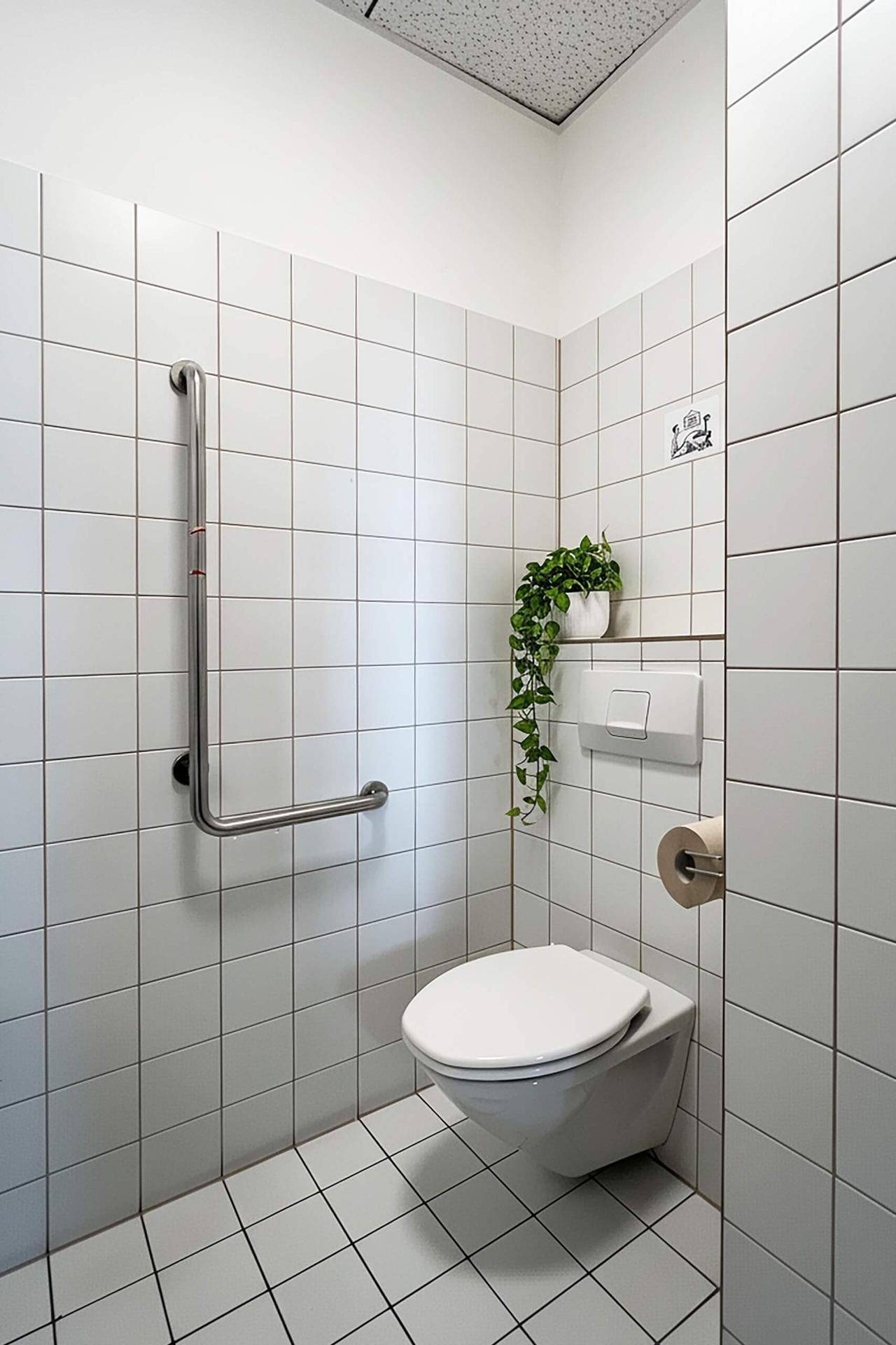 Barrierefreie Toilette mit Wand-WC, Haltegriffen und weißen Fliesen, ausgestattet für Komfort und Sicherheit.