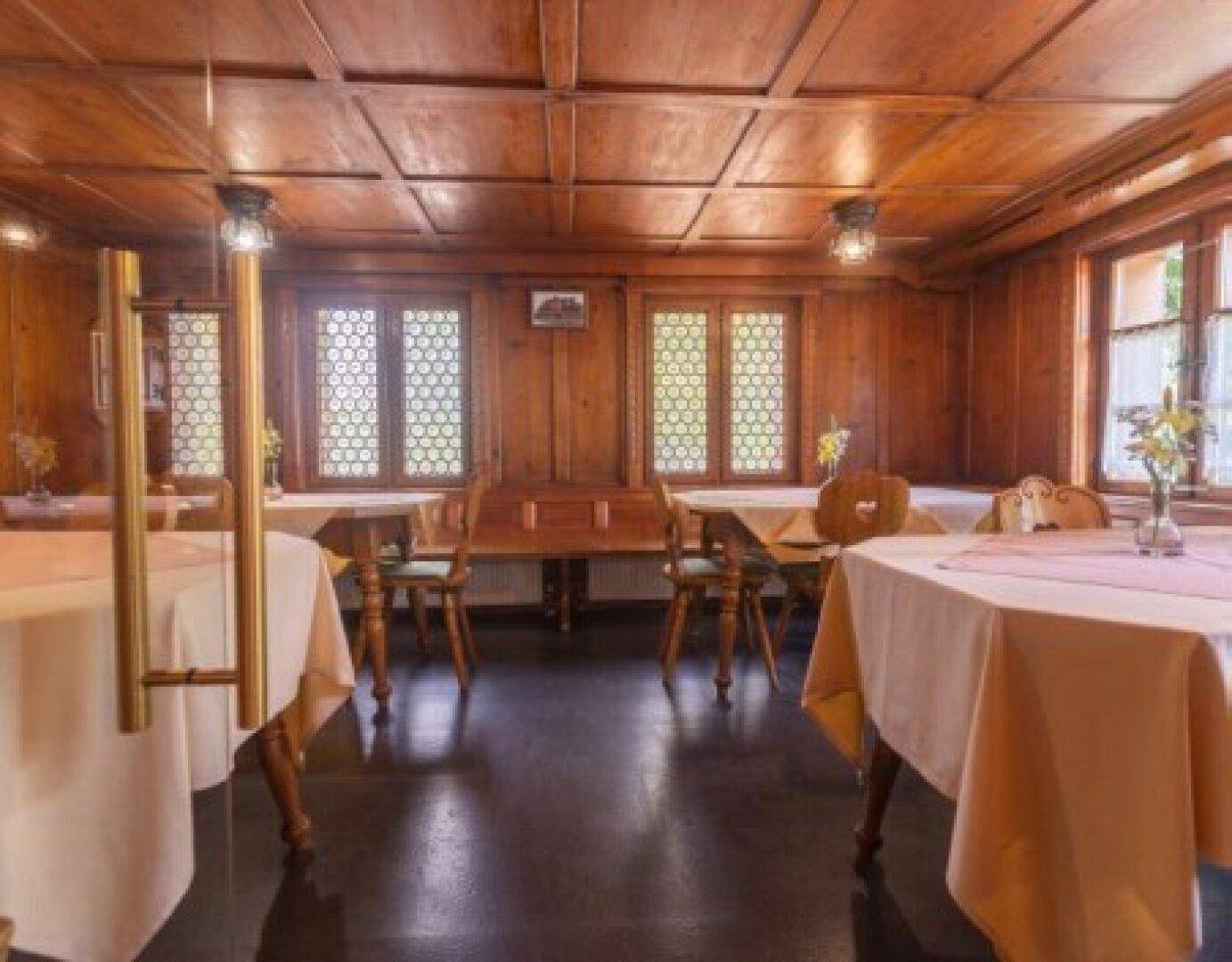 Rustikaler Speisesaal mit dunklem Boden und holzgetäfelten Wänden, bietet eine gemütliche Atmosphäre.