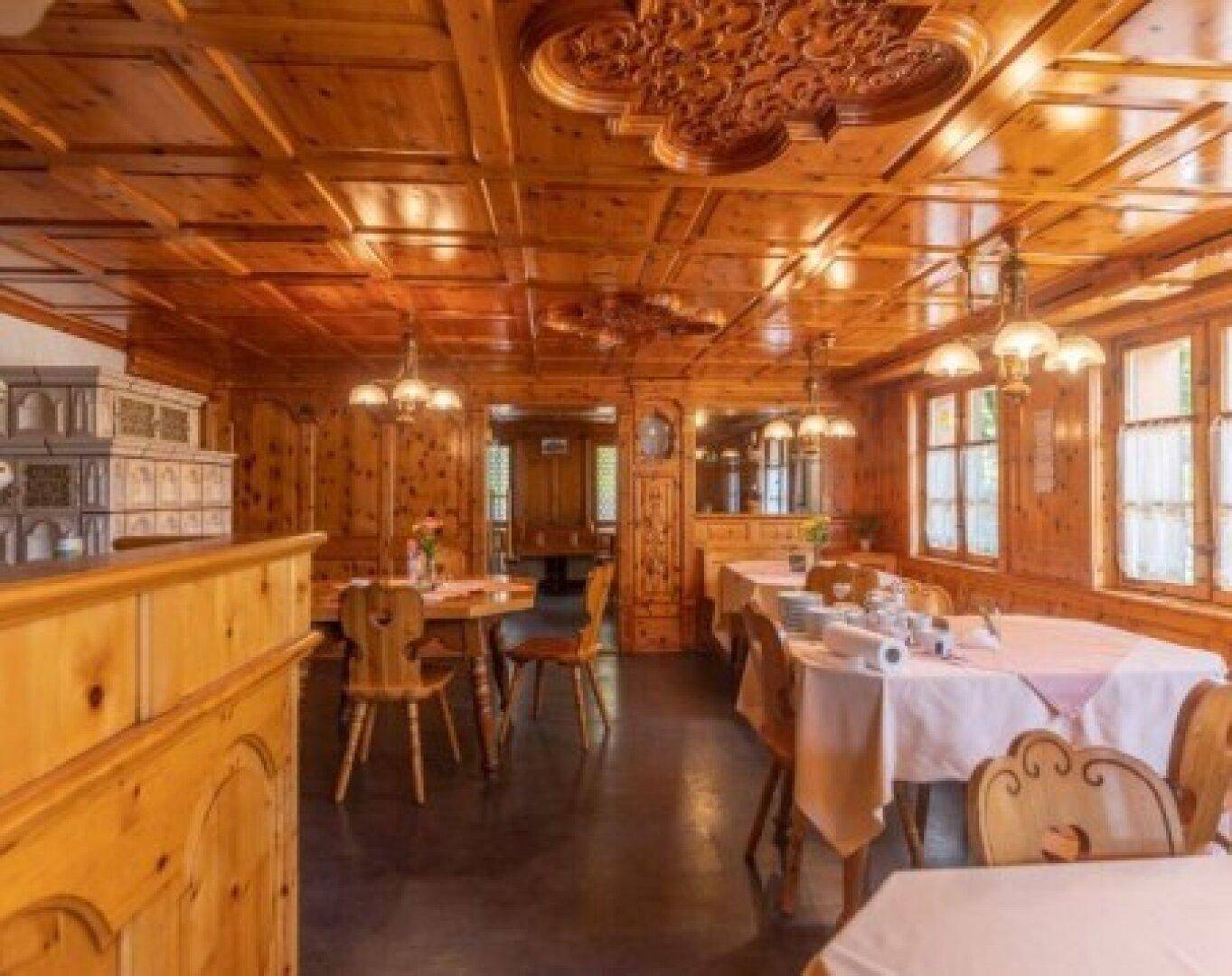 Traditioneller Speisesaal mit holzgetäfelten Wänden und Decken, ausgestattet mit rustikalen Tischen und Stühlen.