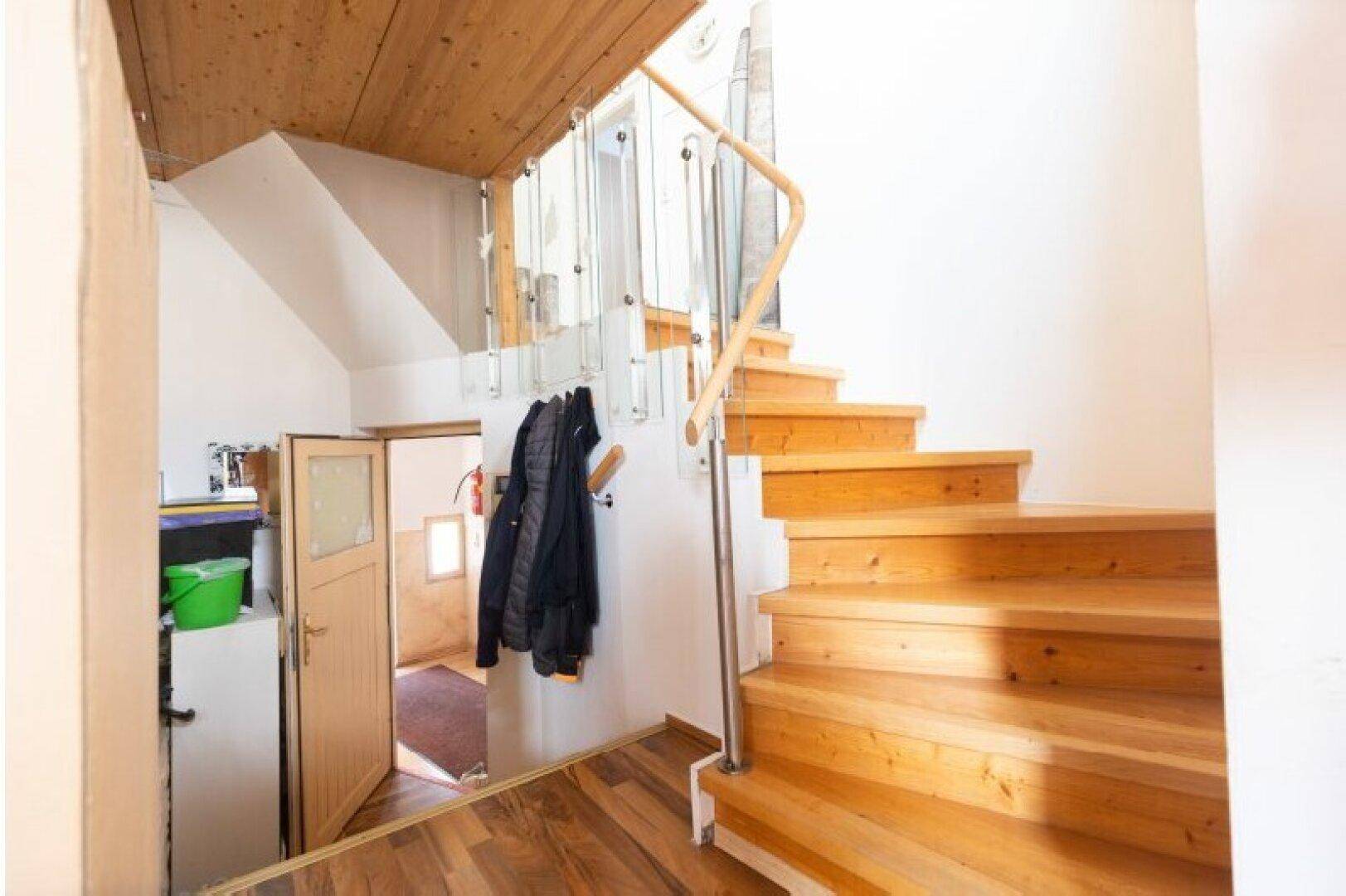 Geräumiger Flur mit Holztreppe und Glasgeländer, der verschiedene Ebenen des Hauses verbindet.