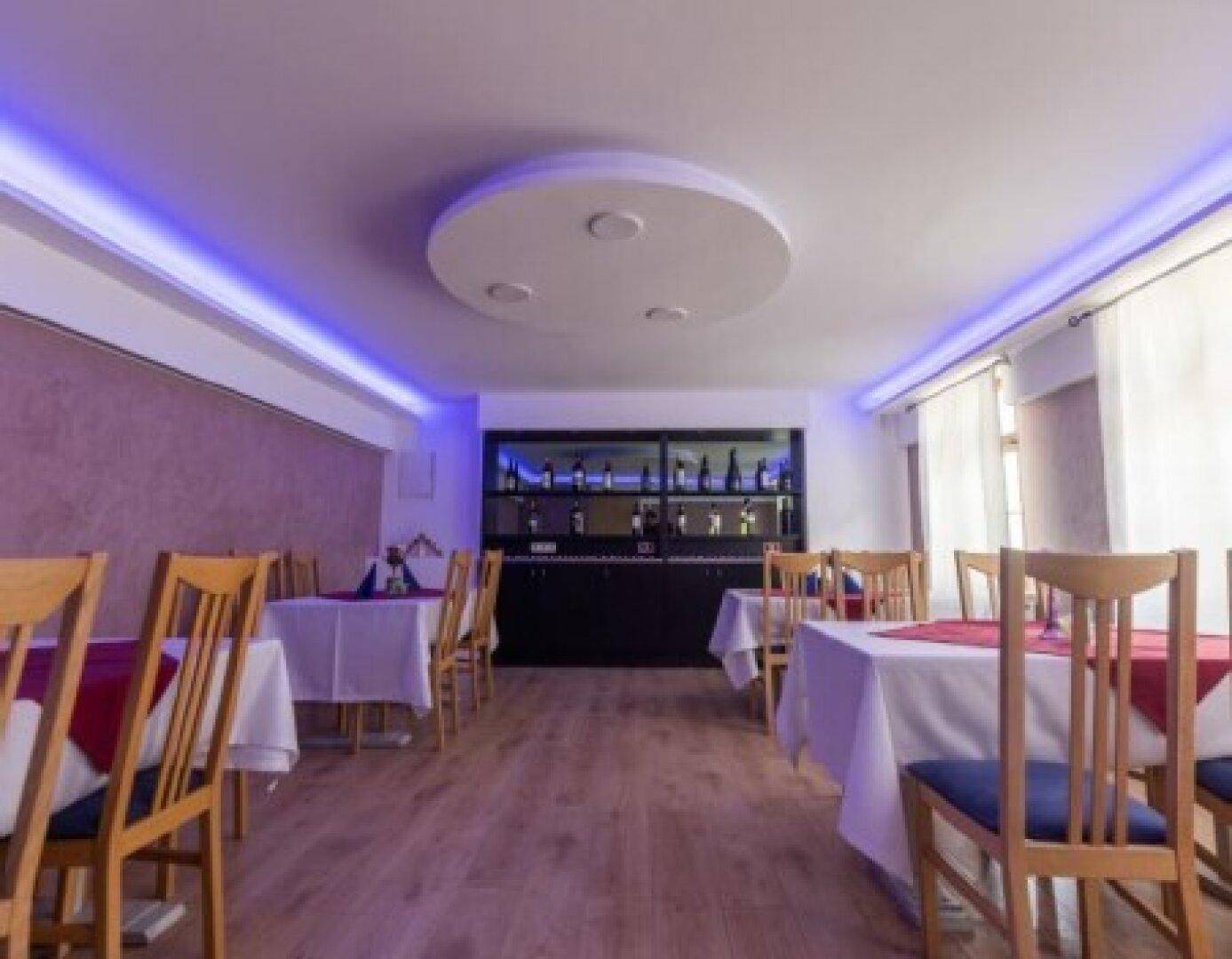 Moderner Speisesaal mit indirekter Beleuchtung und Holzboden, ausgestattet mit eleganten Tischen und Stühlen.