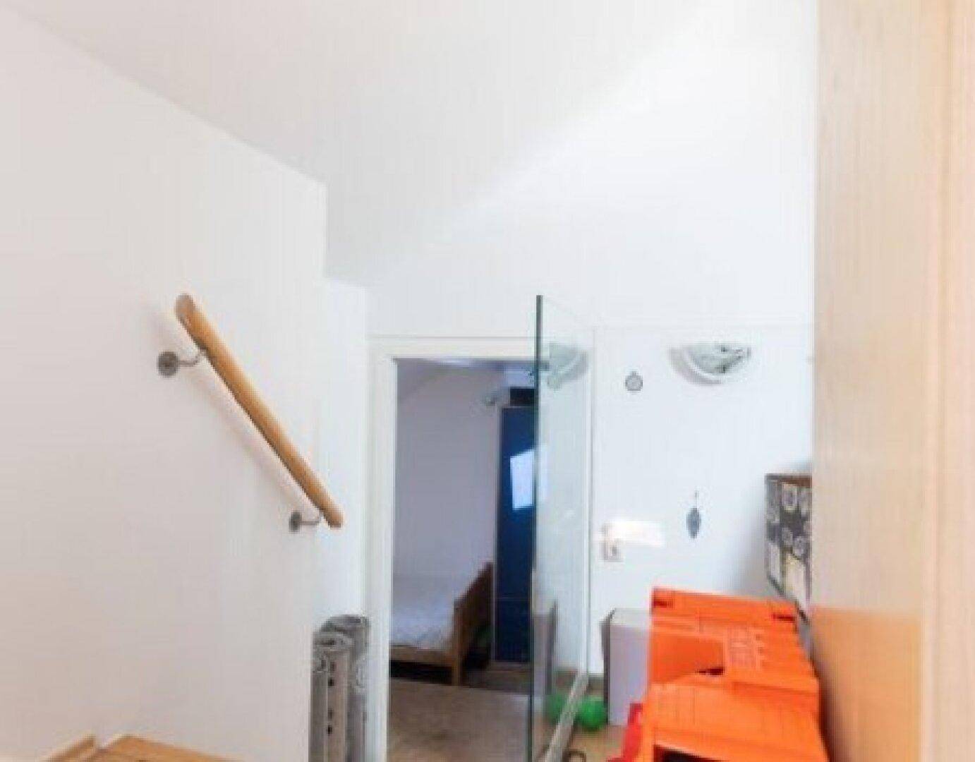Heller Flur mit weiß gestrichenen Wänden und einem Holzhandlauf, der zu weiteren Räumen führt.