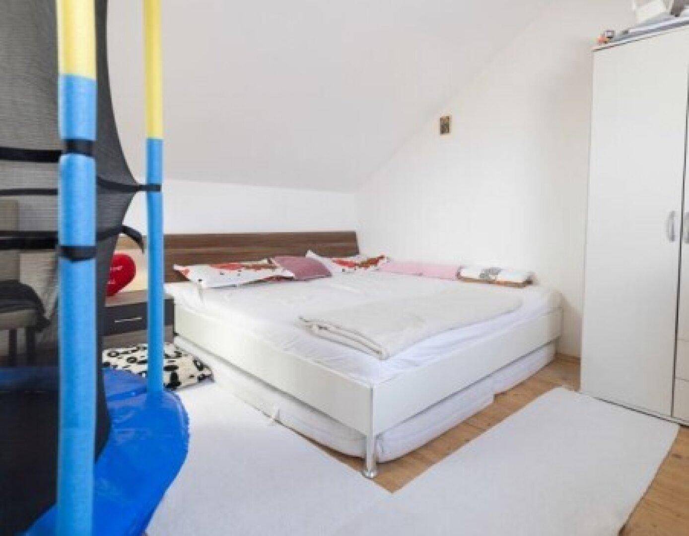 Helles Schlafzimmer im Dachgeschoss mit schrägen Wänden und einem Doppelbett, bietet eine gemütliche Atmosphäre.