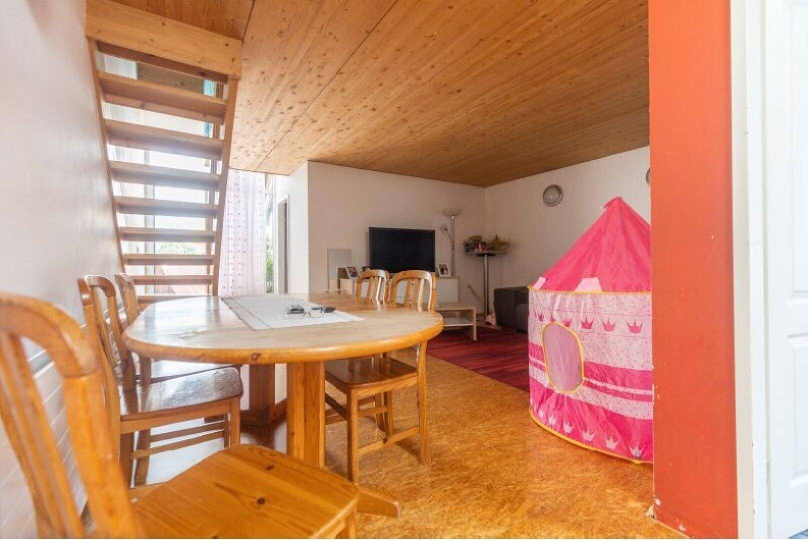 Heller Wohnbereich mit Holzbalkendecke und Laminatboden, ausgestattet mit einem Esstisch und Spielbereich.