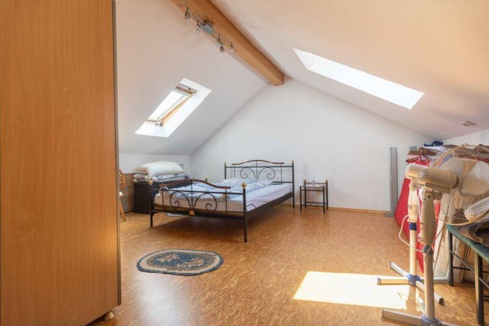 Geräumiges Schlafzimmer im Dachgeschoss mit zwei Dachfenstern und Holzbalken, bietet viel Tageslicht.
