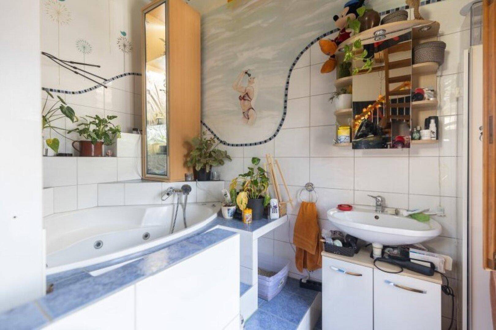 Buntes Badezimmer mit Badewanne und Waschbecken, dekoriert mit Pflanzen und Wandmalereien.