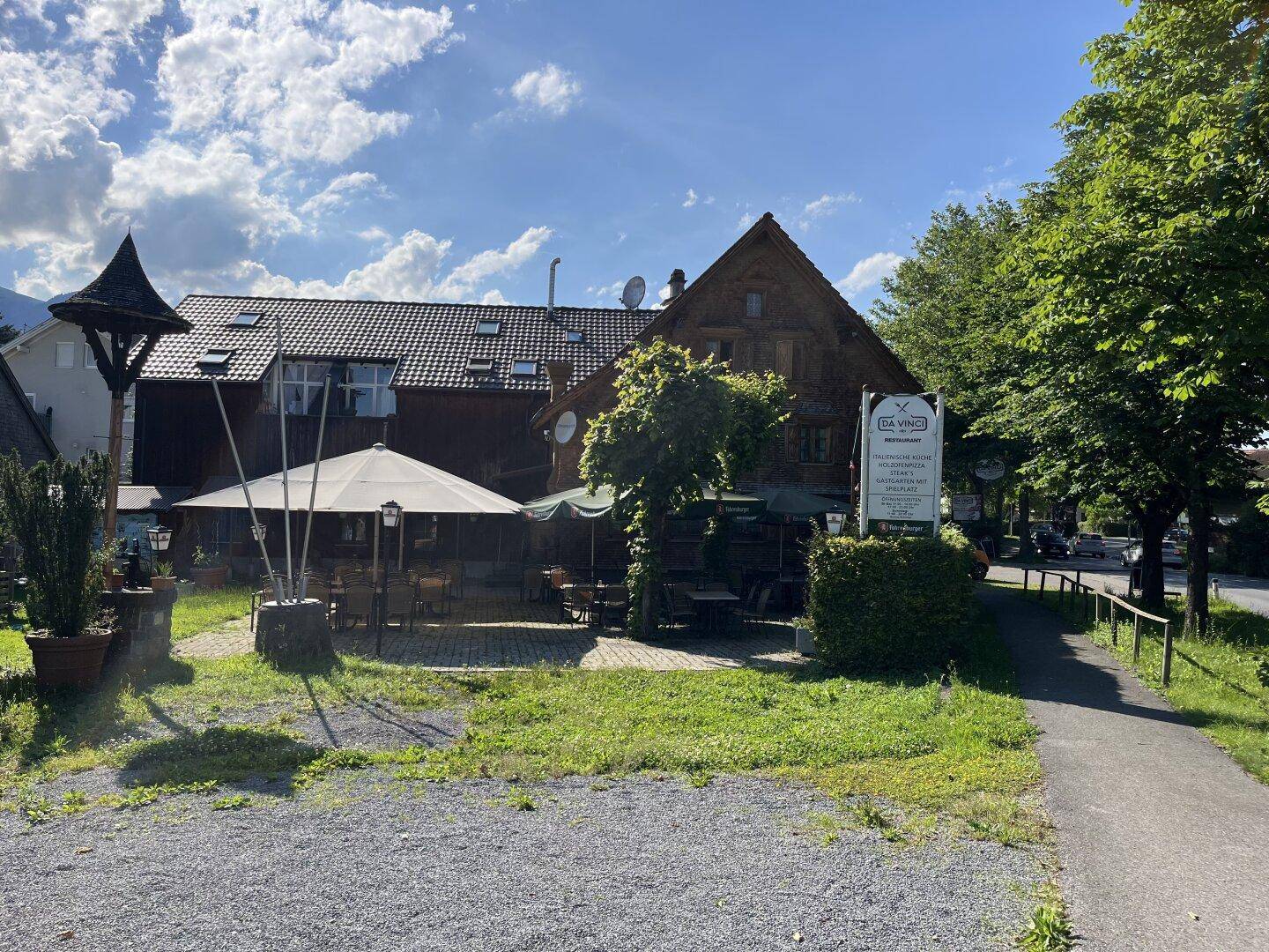 Gemütlicher Außenbereich mit Sonnenschirmen und Sitzgelegenheiten, umgeben von Bäumen und Grünflächen.