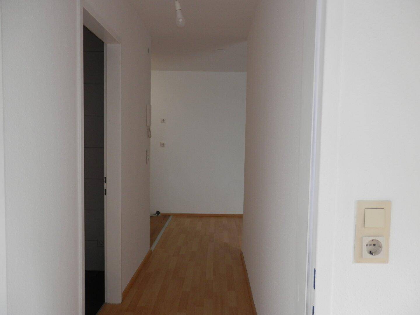 Heller Flur mit Laminatboden und weiß gestrichenen Wänden, der zu weiteren Räumen führt.