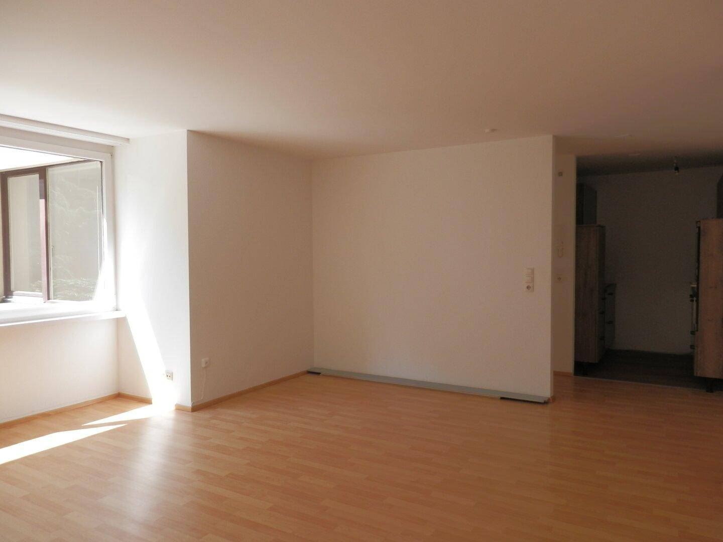 Geräumiges Wohnzimmer mit Laminatboden und viel Tageslicht durch ein großes Fenster.