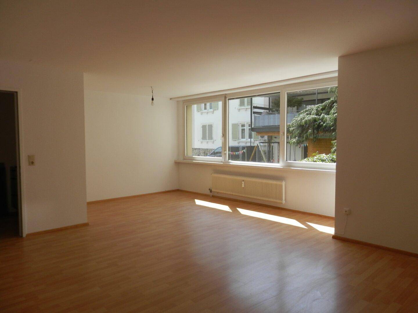 Helles Wohnzimmer mit Laminatboden, großem Fenster und Blick auf die Umgebung.