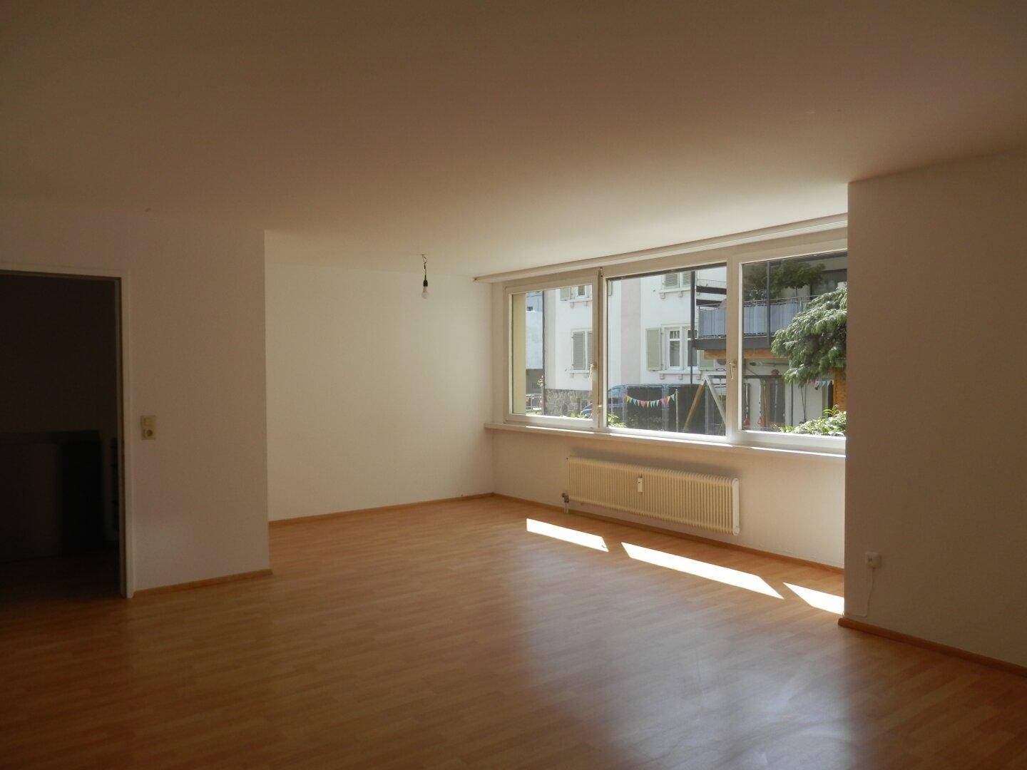Lichtdurchflutetes Wohnzimmer mit Laminatboden und breiter Fensterfront, die viel Helligkeit spendet.