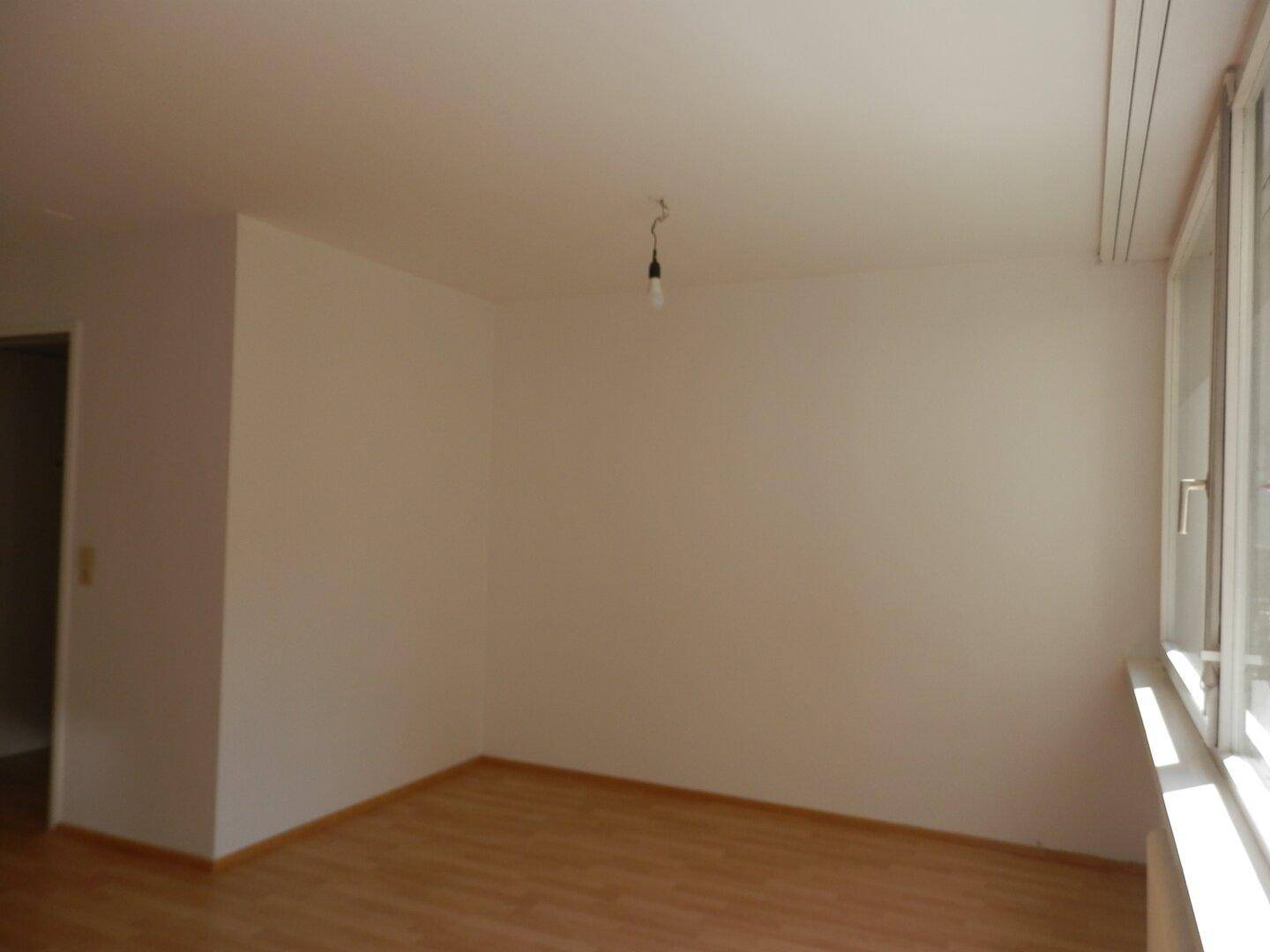 Heller Wohnbereich mit Laminatboden und großem Fenster, das den Raum mit Tageslicht füllt.
