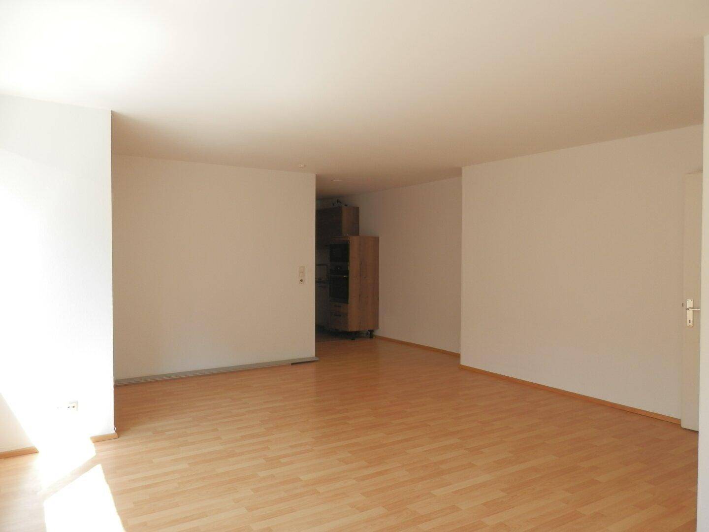 Geräumiges Wohnzimmer mit Laminatboden und weiß gestrichenen Wänden, bereit zur individuellen Gestaltung.