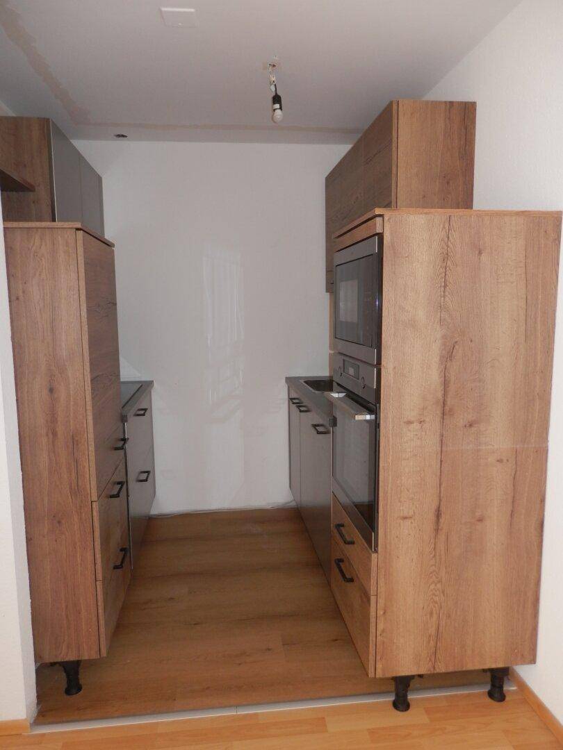 Schmale Küche mit Holzoptik-Schränken und integrierten Geräten, die auf beiden Seiten angeordnet sind.