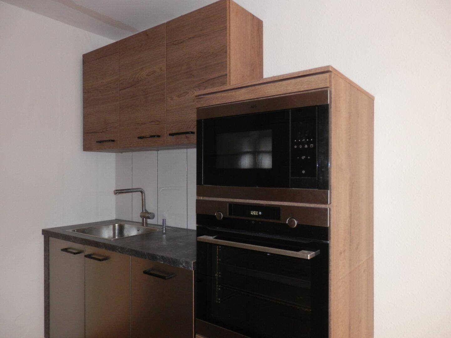 Moderne Küche mit Spüle, Backofen und Mikrowelle in Holzoptik-Schränken integriert.
