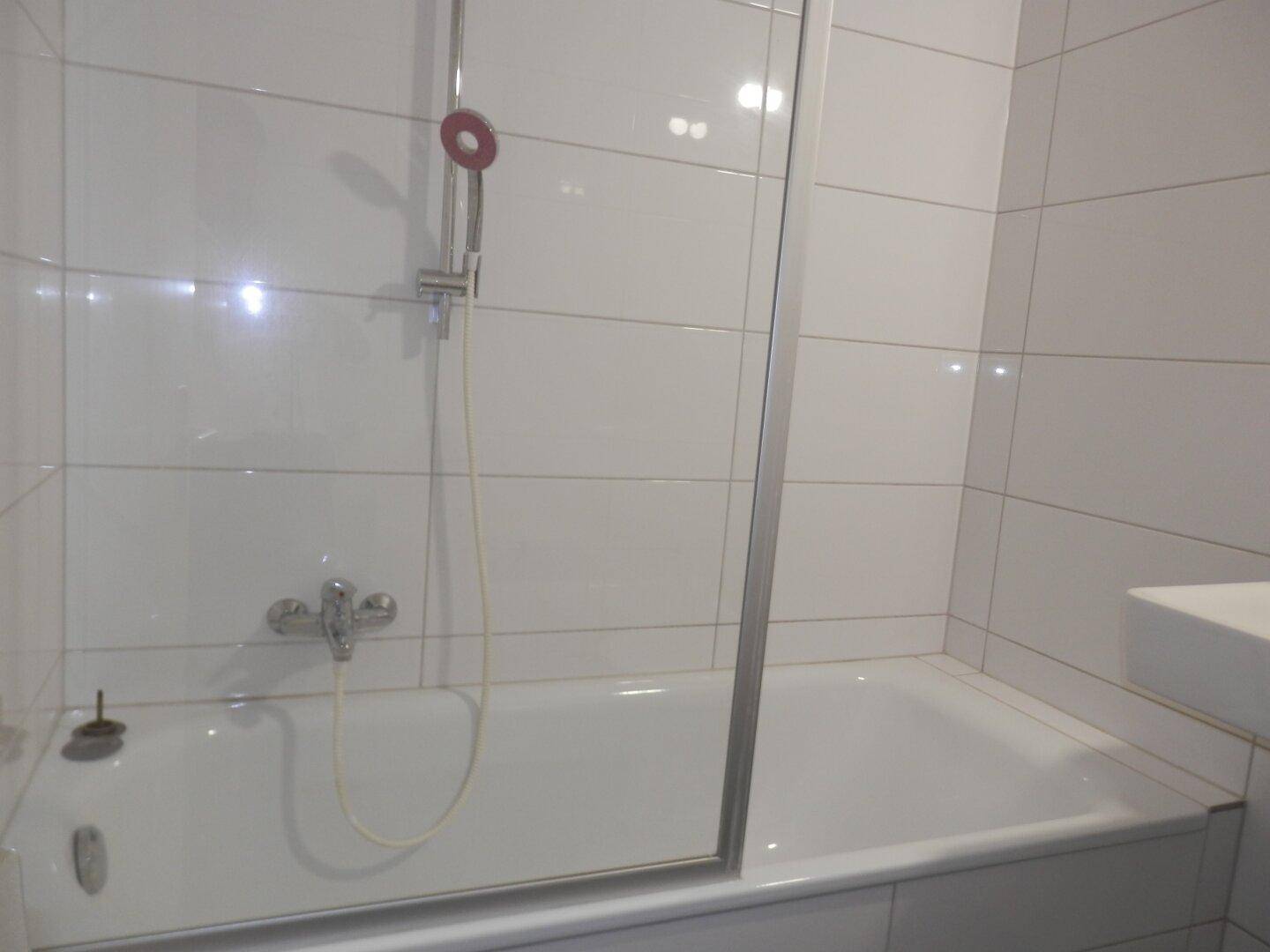 Badezimmer mit weiß gefliester Wand, Badewanne und Duschkopf, bereit zur Nutzung.