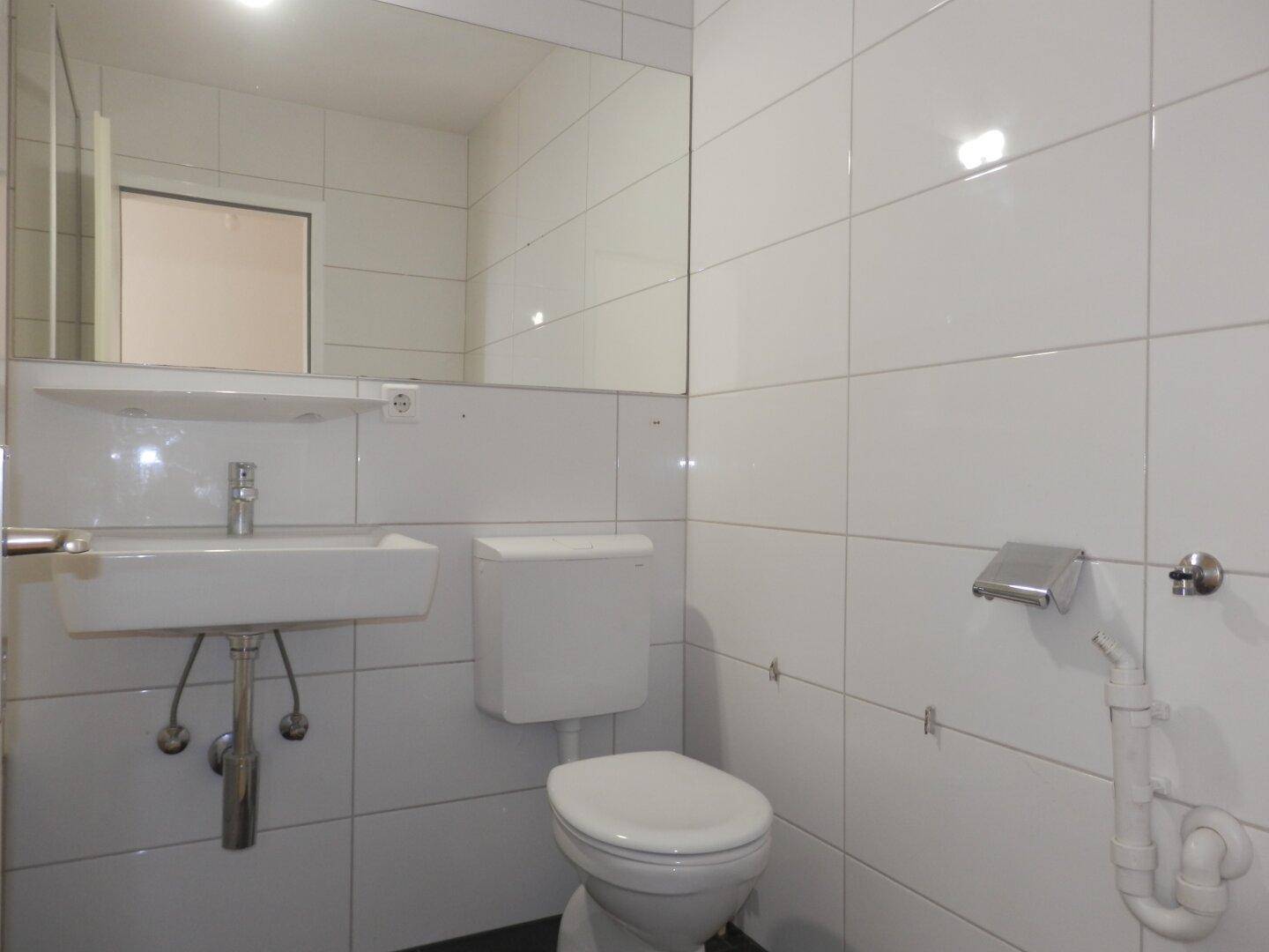 Modernes WC mit weißen Fliesen, wandmontiertem Spiegel und kleinem Waschbecken.