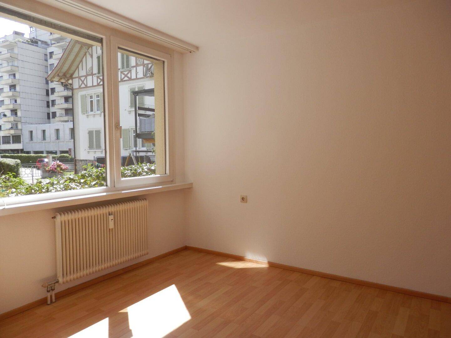 Helles Schlafzimmer mit Laminatboden und großem Fenster, das viel Tageslicht hereinlässt.