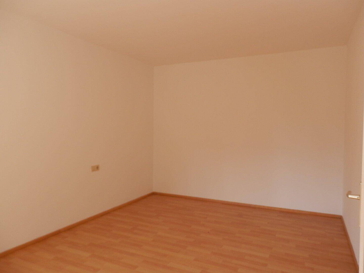 Leeres Schlafzimmer mit Laminatboden und weißen Wänden, ideal für individuelle Einrichtung.